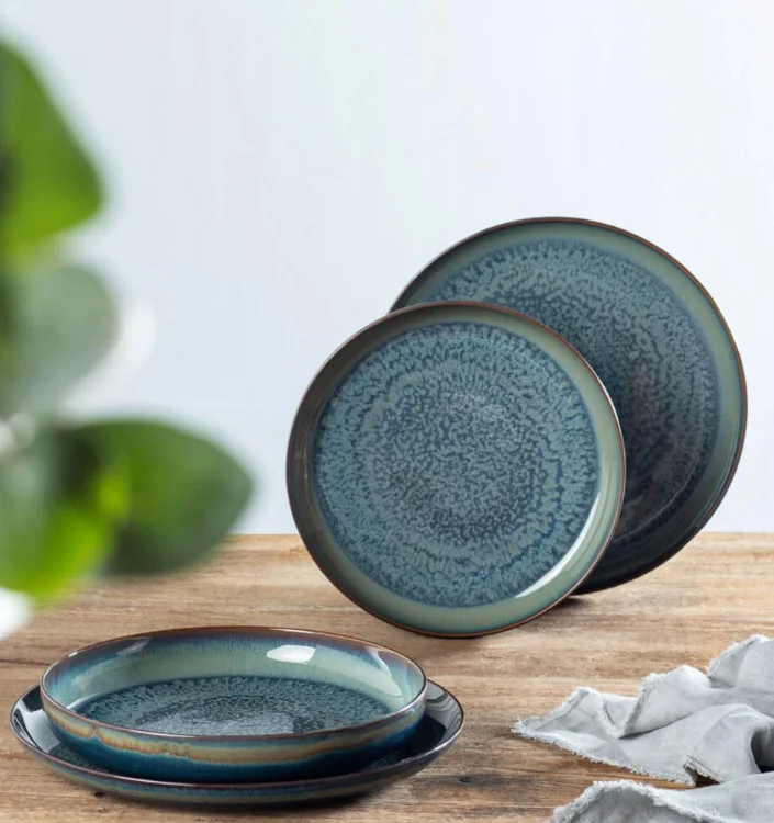 Blau-grünes Steingut-Tellerset mit reaktiver Glasur und organischem Rand auf Holztisch mit Stoffserviette.