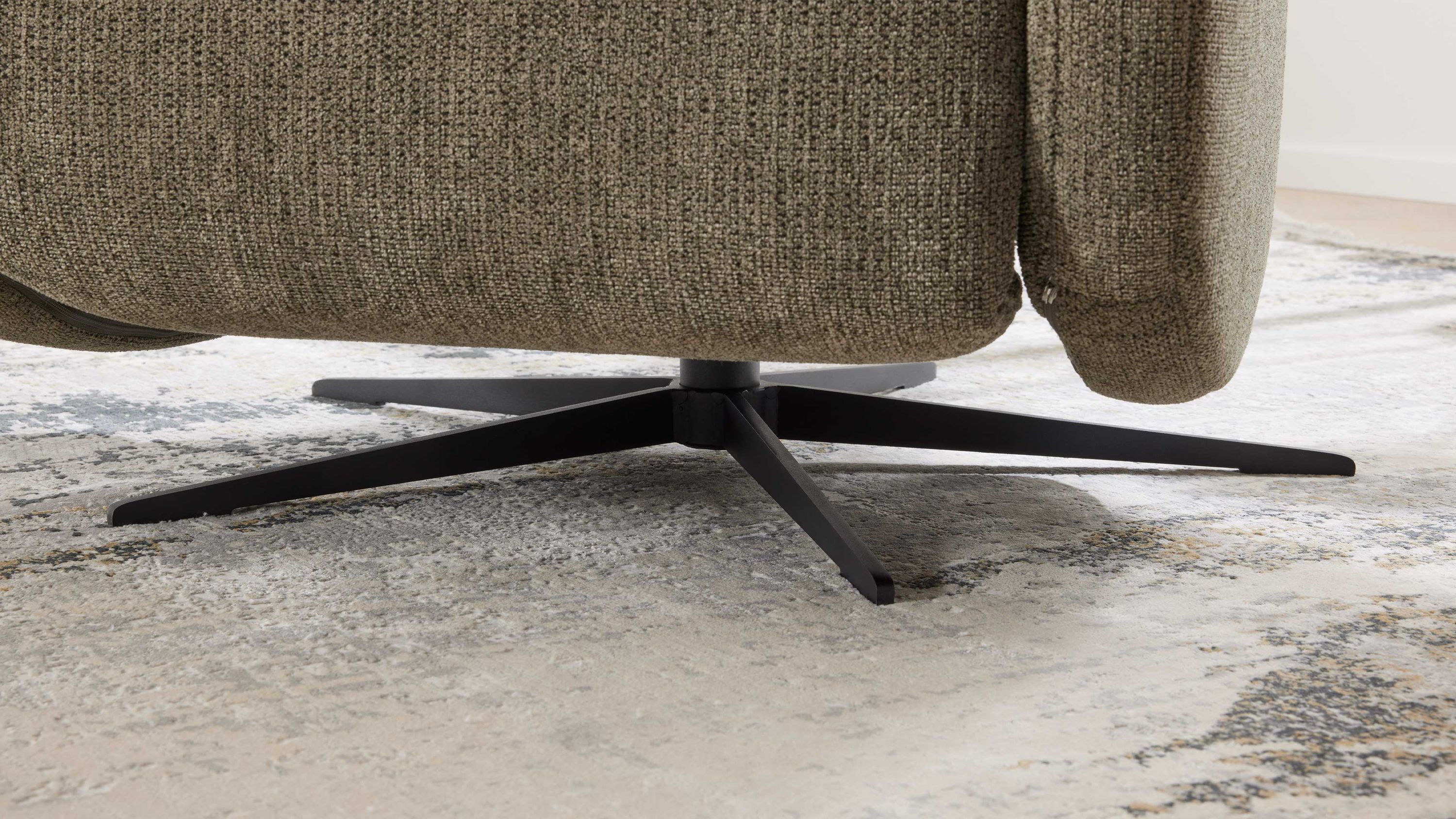 Schwarzer Kreuzfuß aus Metall unter einem graubraunen Polstersessel auf Teppichboden