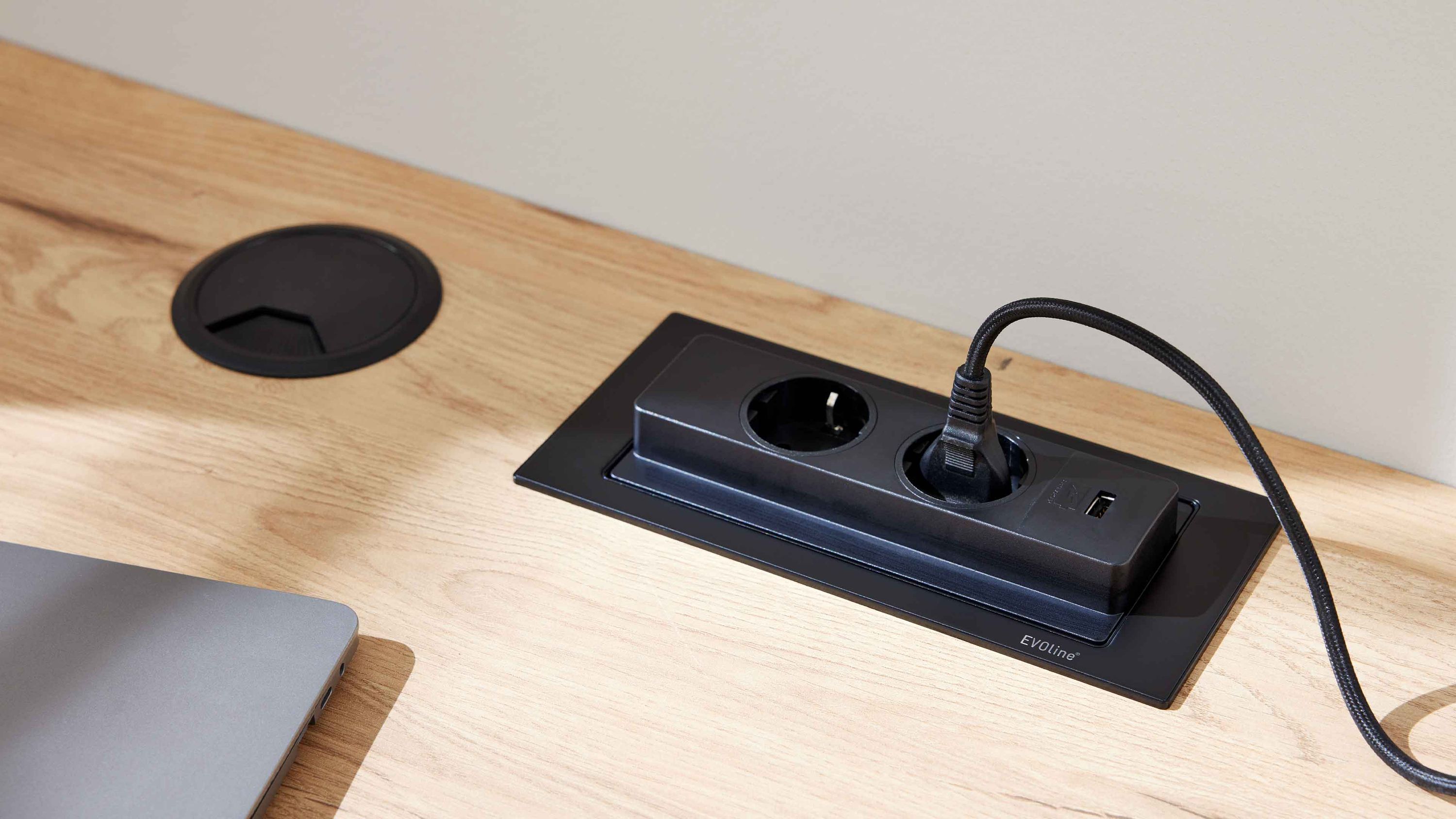 Schreibtisch mit integriertem schwarzen Steckdosenmodul und Laptop auf hellem Holz