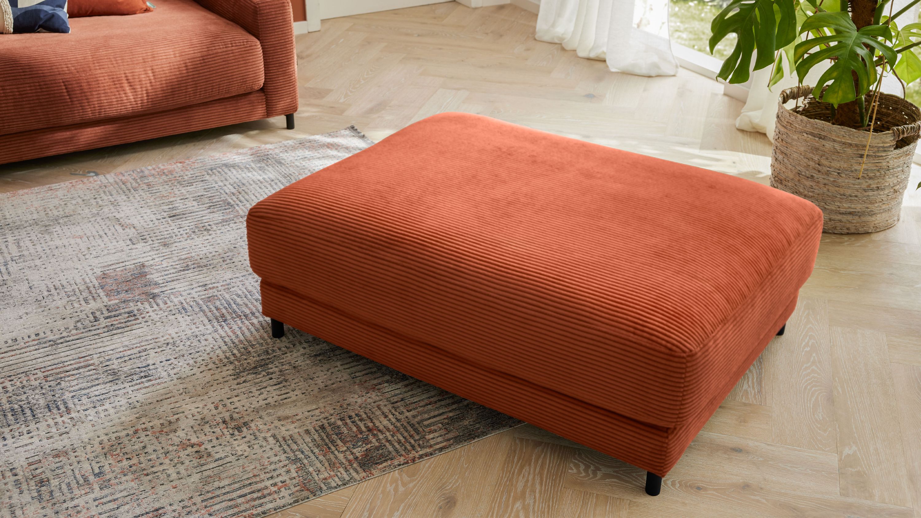 XXL-Polsterhocker in rostrot mit Metallfüßen Großer rechteckiger Polsterhocker in rostrot mit Metallfüßen auf hellem Holzboden