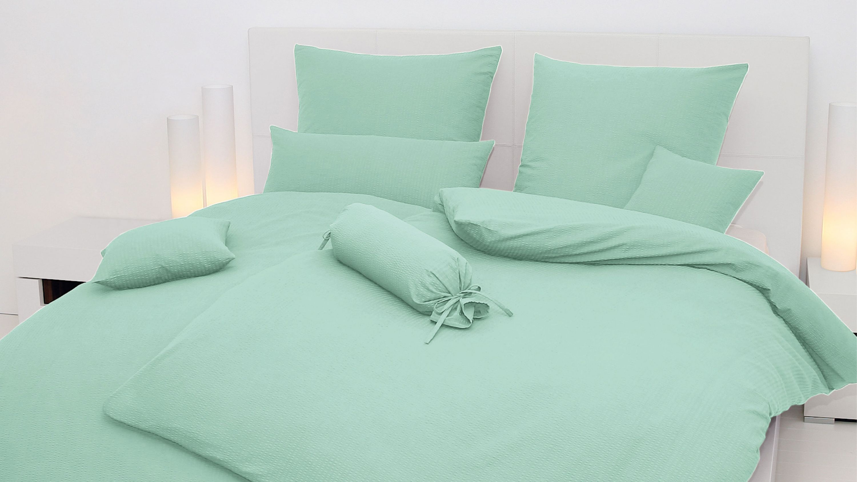 Hellgrünes Bettwäsche-Set mit Kissen und Zierrolle auf weißem Bett mit Kopfteil