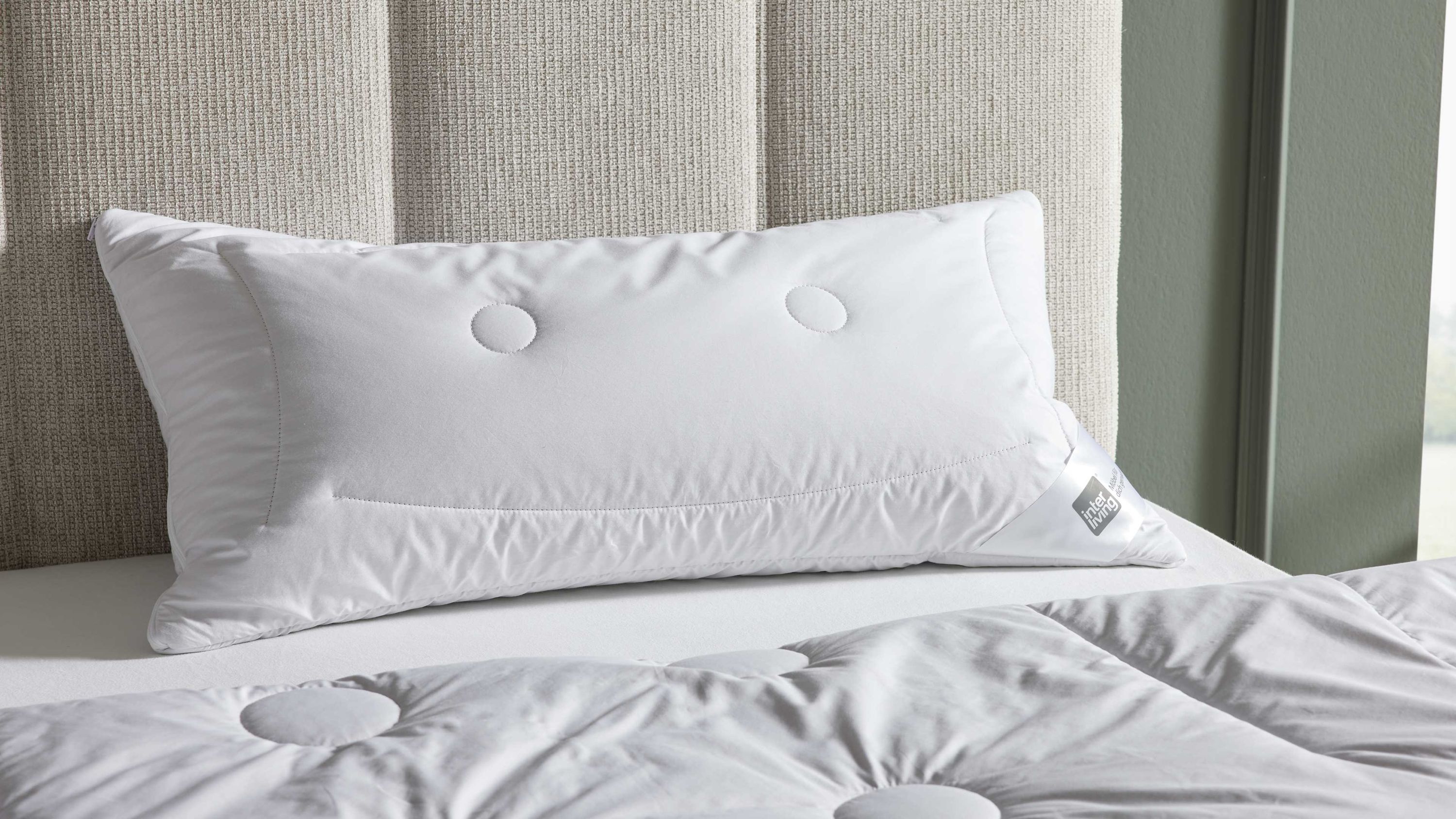 Rechteckiges weißes Kopfkissen mit zwei runden Steppungen auf einem Bett mit weißer Bettdecke