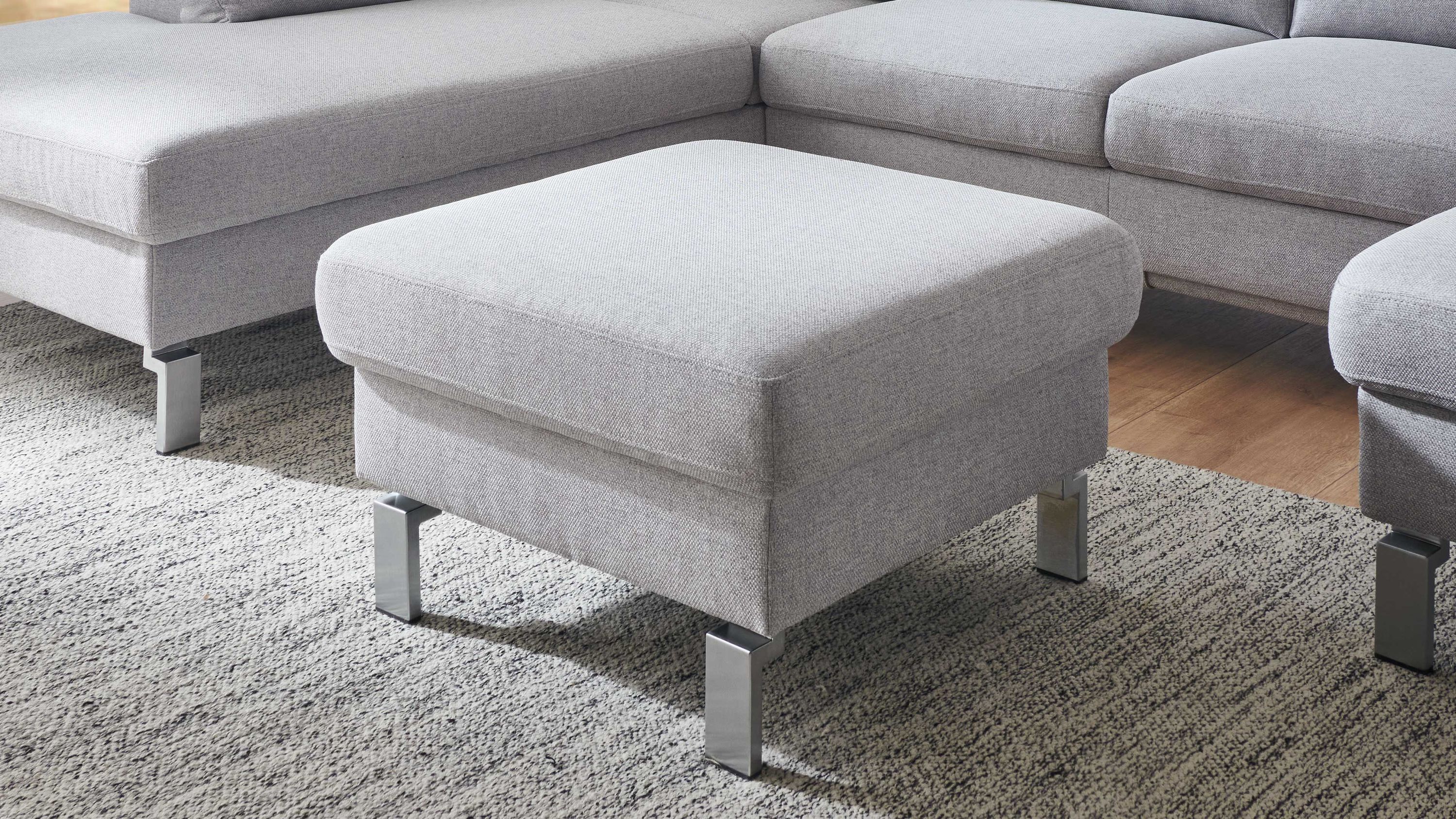 Quadratischer Polsterhocker mit hellgrauem Flachgewebe und Metallfüßen auf Teppichboden