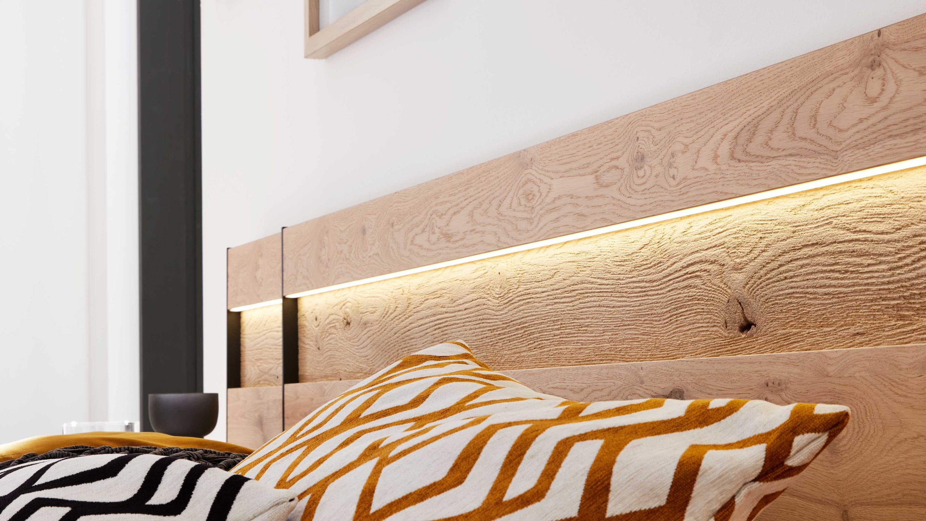Holzkopfteil mit LED-Beleuchtung und gemusterten Kissen Holzkopfteil mit integrierter LED-Beleuchtung über dem Bett mit gemusterten Kissen in Weiß und Braun