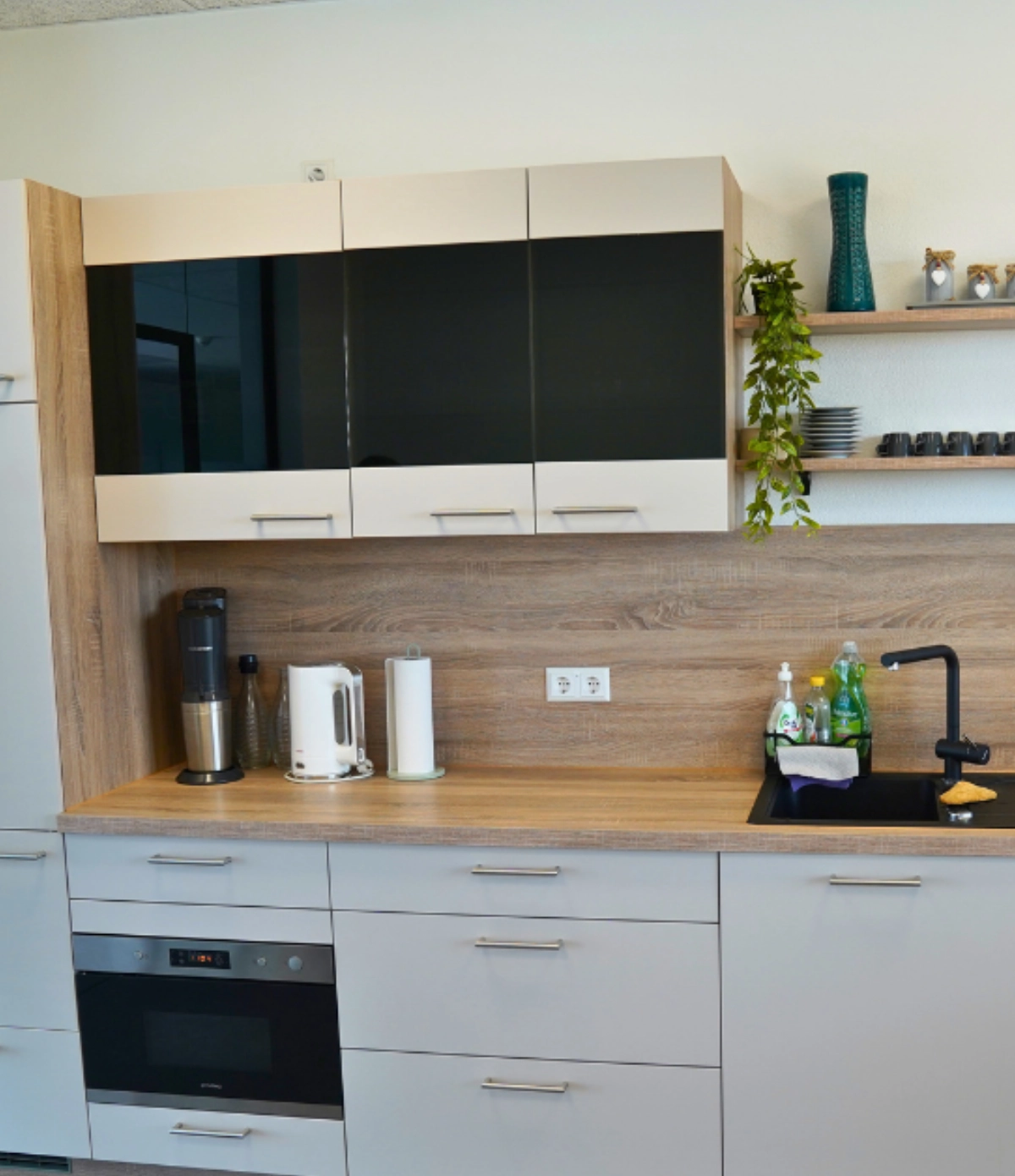 Moderne Büroküche mit Oberschränken, Holzarbeitsplatte, Spüle, Einbaugeräten und Kaffeemaschine, funktionaler Pausenbereich im Büro