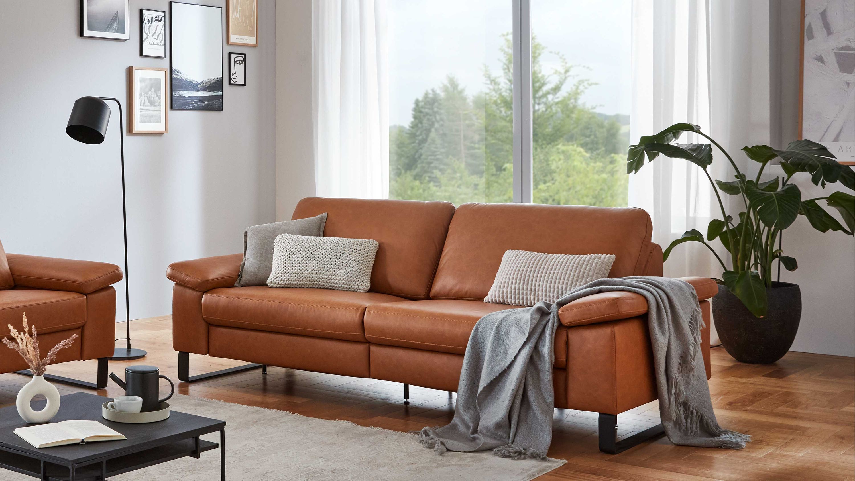 Dreisitziges Sofa aus cognacfarbenem Leder mit schwarzen Metallfüßen und zwei grauen Kissen