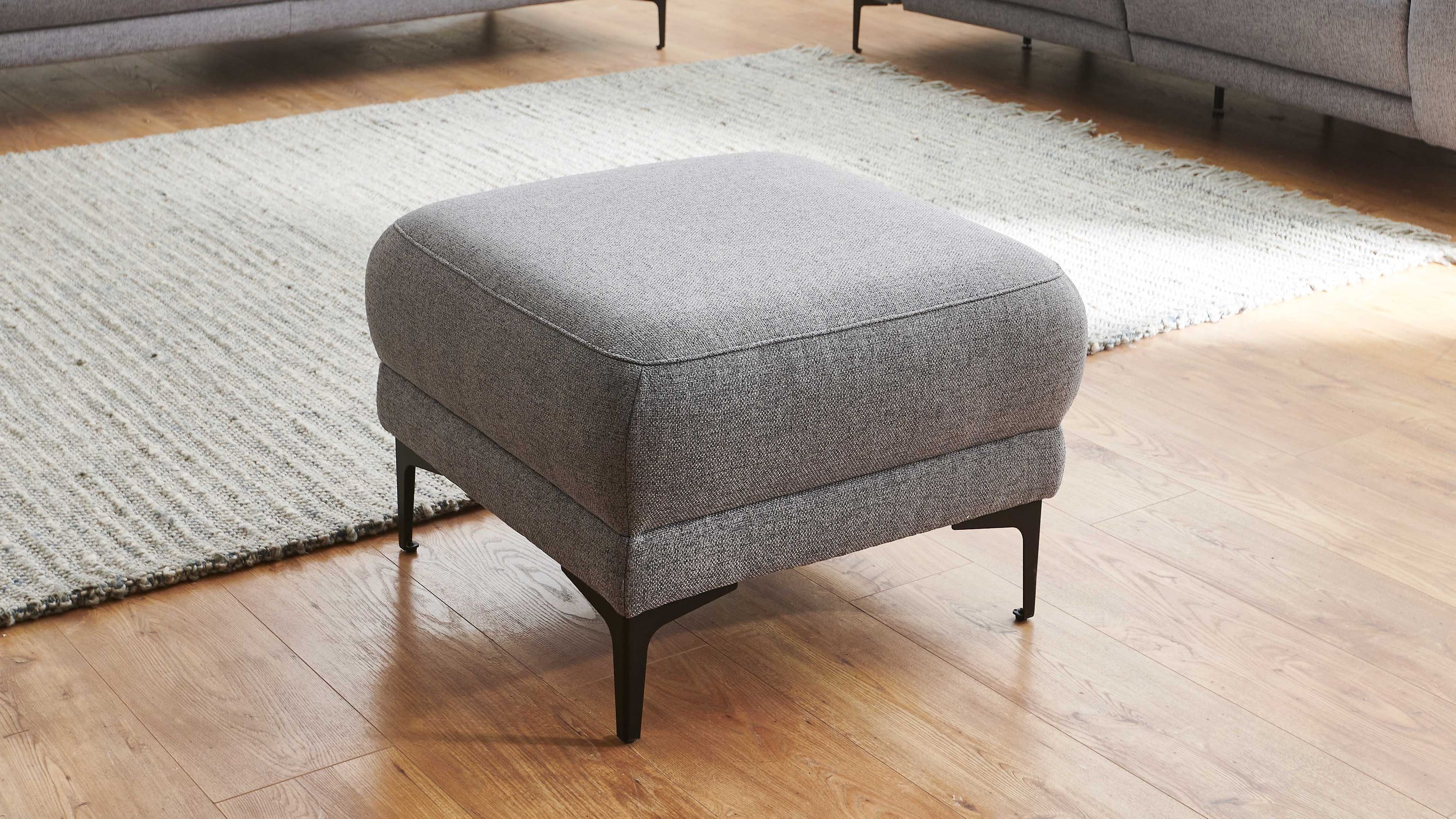 Polsterhocker quadratisch mit grauem Bezug und schwarzen Winkelfüßen Quadratischer Polsterhocker mit grauem Flachgewebe und schwarzen Winkelfüßen auf Holzboden