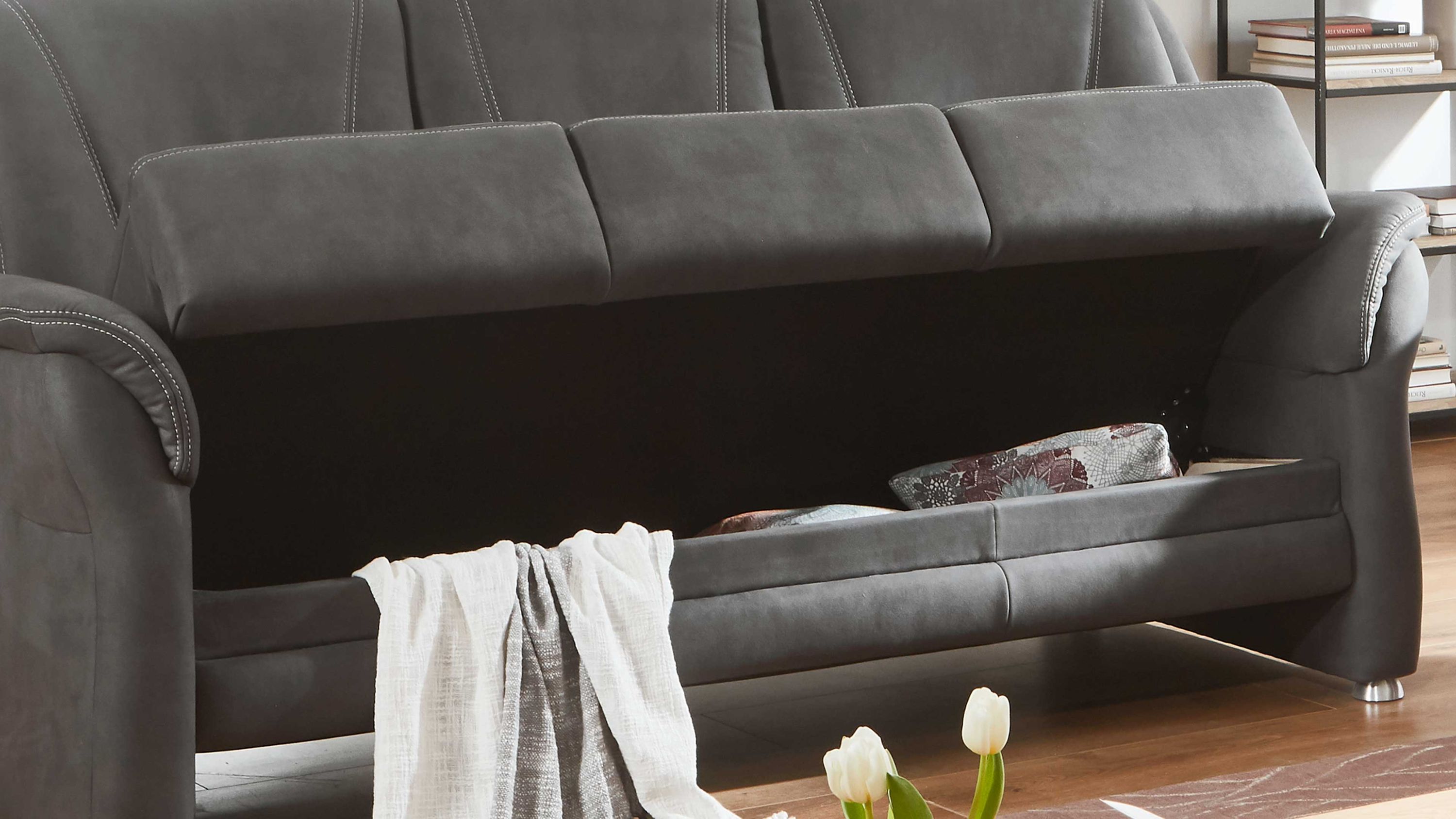 Dreisitziges Sofa in dunkelgrauer Farbe mit geöffnetem Bettkasten und Decke sowie Kissen darin