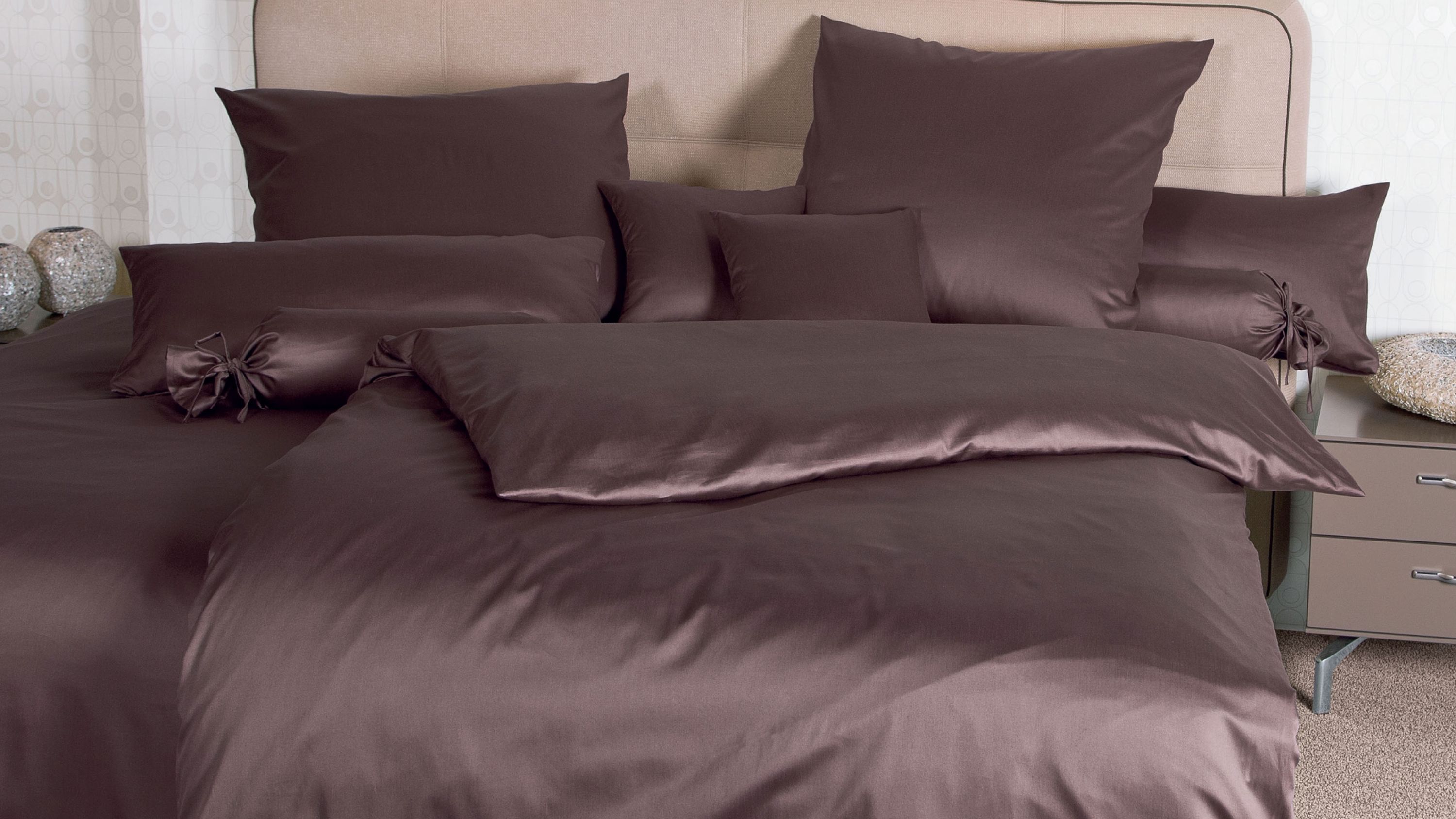 Braunes Bettwäsche-Set mit mehreren Kissen und Zierkissen auf einem Bett mit gepolstertem Kopfteil