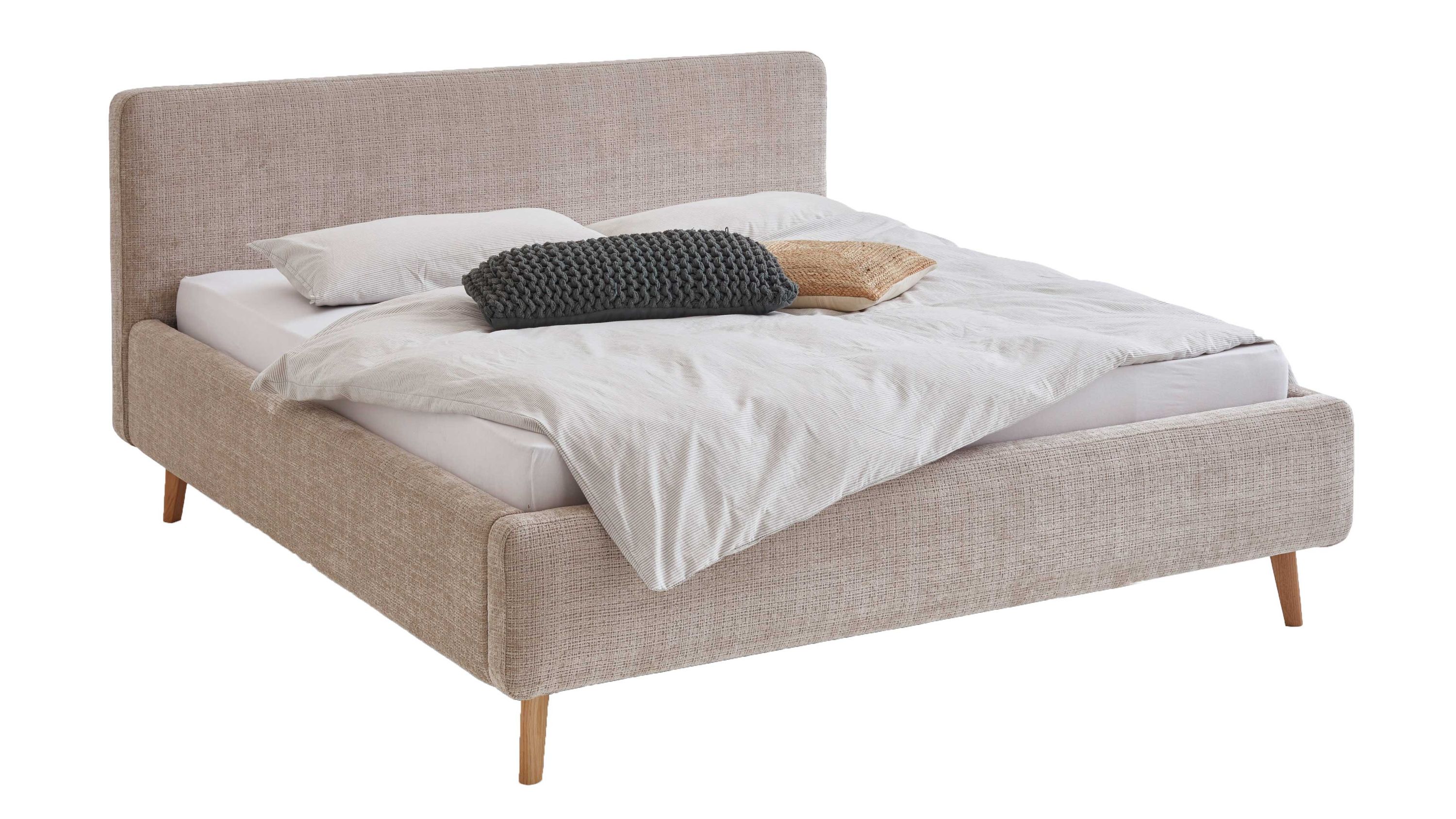 Polsterbett mit Holzfüßen und beigefarbenem Bezug Beigefarbenes Polsterbett mit rechteckigem Kopfteil und Holzfüßen mit Bettdecke und Kissen belegt