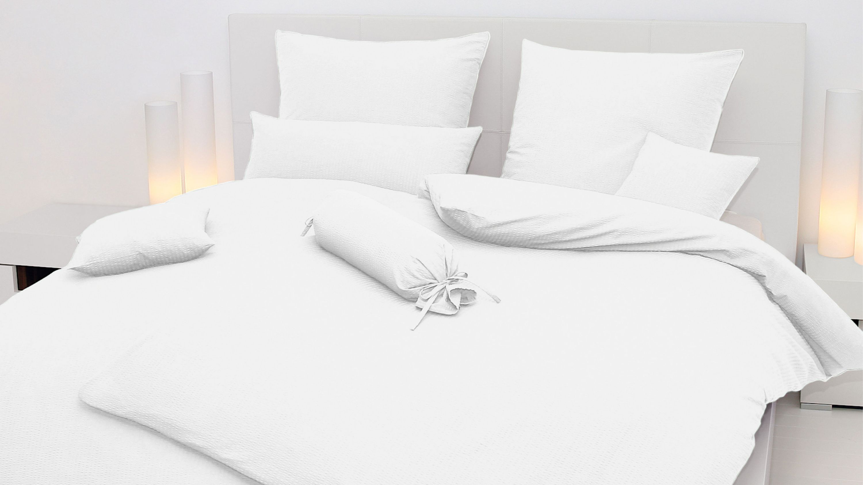 Weißes Bettwäsche-Set mit Kissen und Decke auf hellgrauem Bett mit Kopfteil