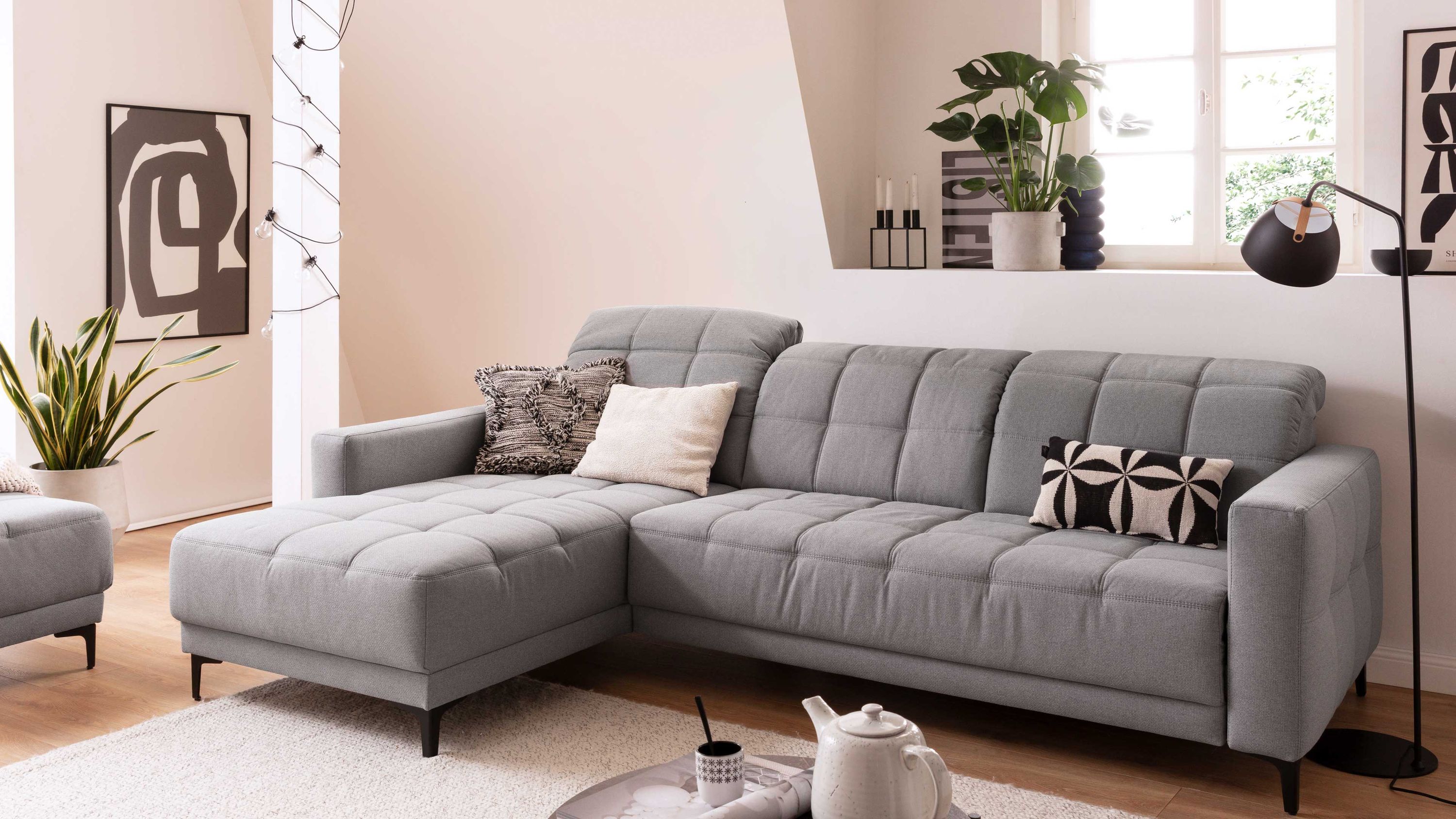 Ecksofa mit silbergrauem Stoffbezug und schwarzen Metallfüßen in modernem Wohnzimmer mit Kissen