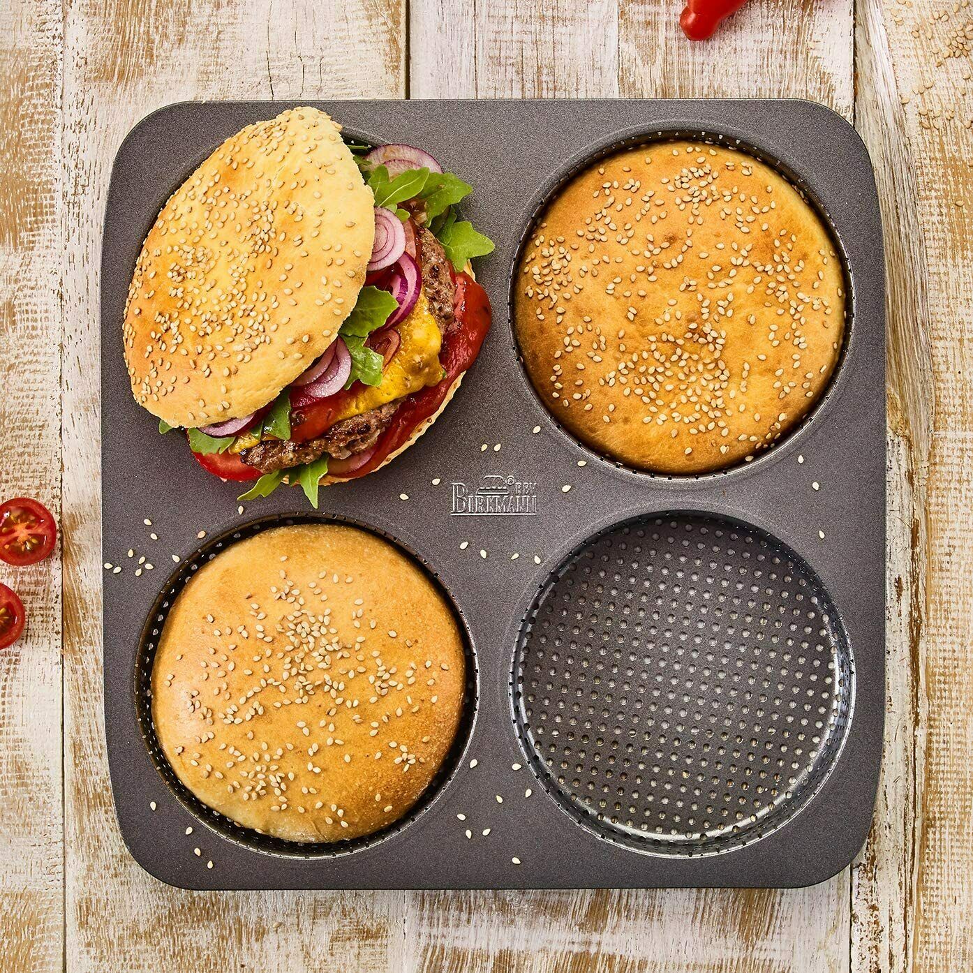 Stahlbackform mit vier runden Mulden  drei mit Burgerbrötchen belegt  ein fertiger Burger mit Belag daneben platziert