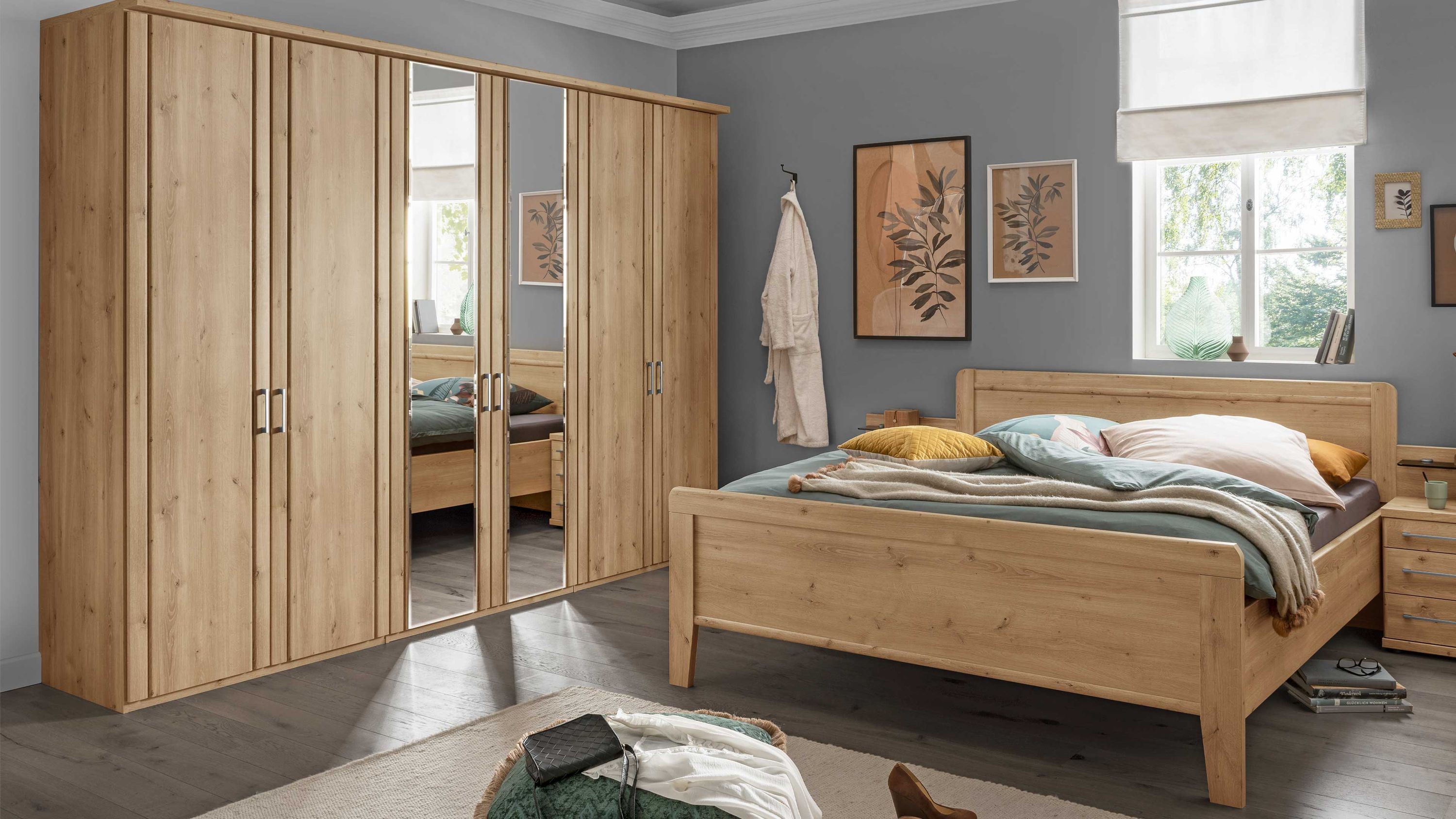 Schlafzimmer mit Holzbett und großem Kleiderschrank mit Spiegeln in hellem Holzton