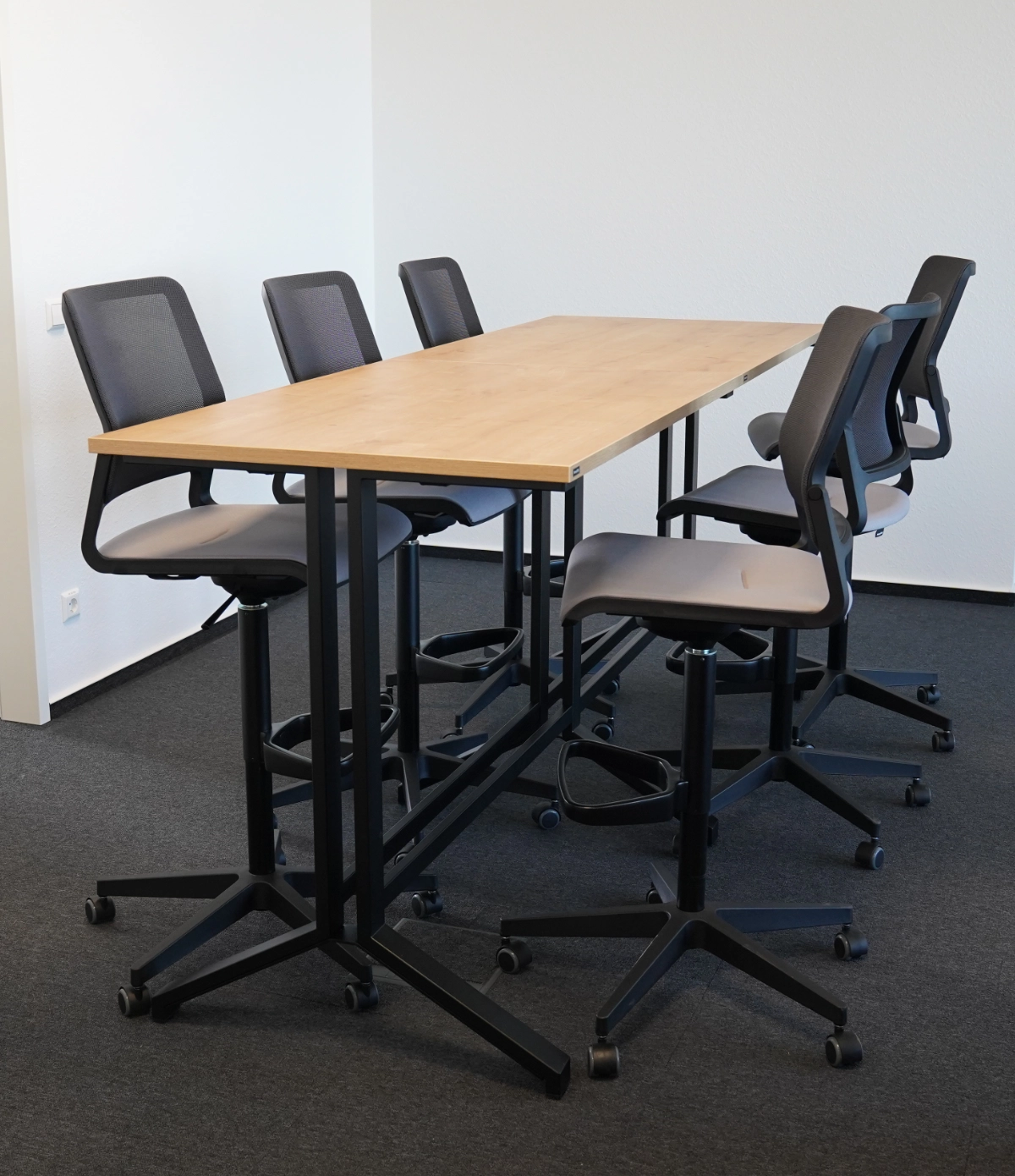 Hoher Besprechungstisch mit Barhockern und Rollstühlen auf Teppichboden, moderner Meetingbereich im Bürodesign