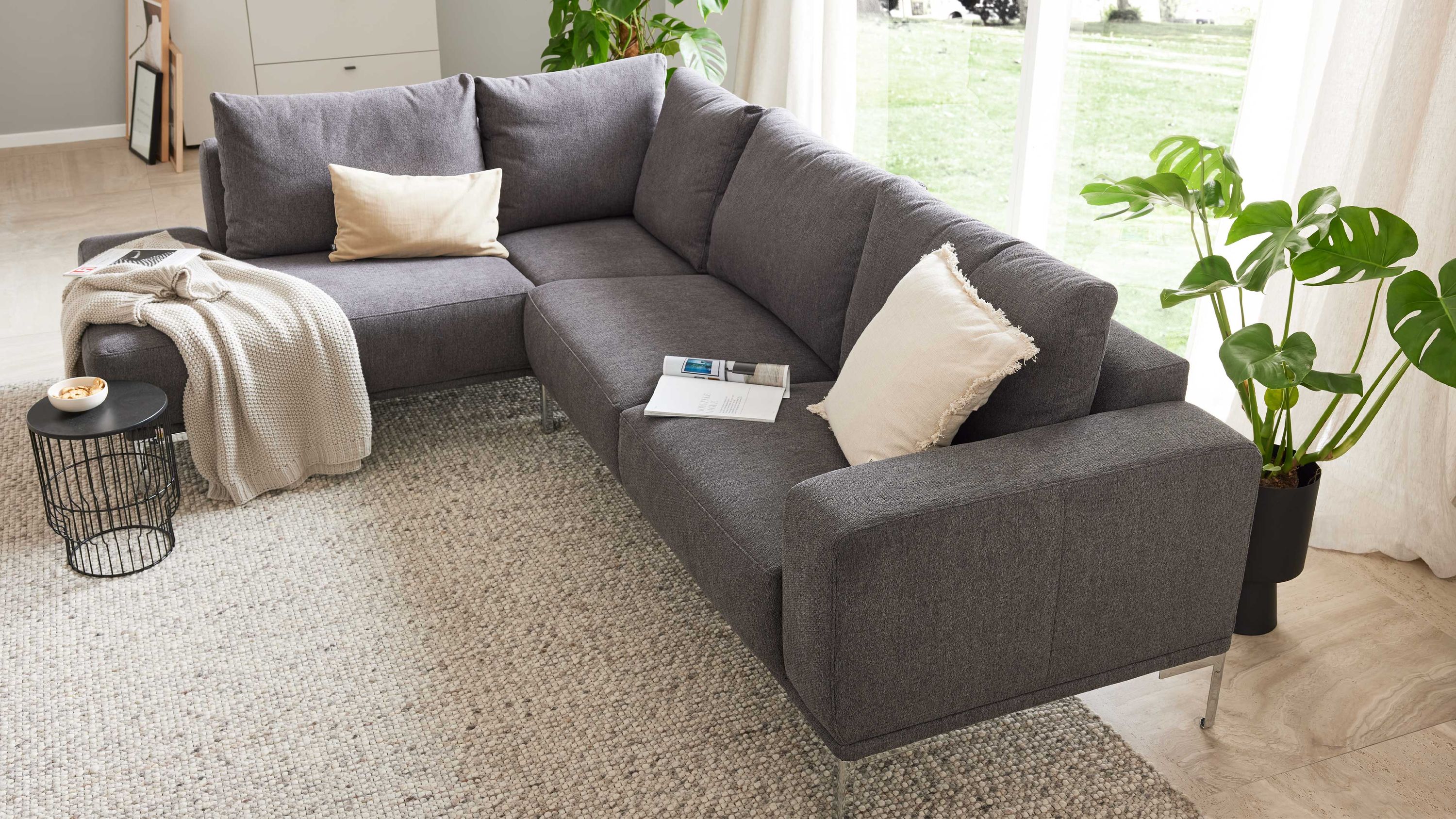 Ecksofa mit grauem Stoffbezug silberfarbenen Metallfüßen und zwei hellen Kissen in modernem Wohnzimmer