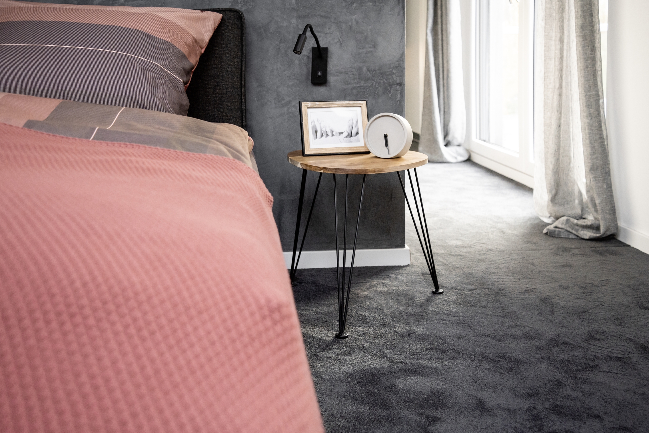 Beistelltisch mit Holzplatte und Metallbeinen neben Bett mit rosa-grauer Bettwäsche Bildrahmen und Wecker
