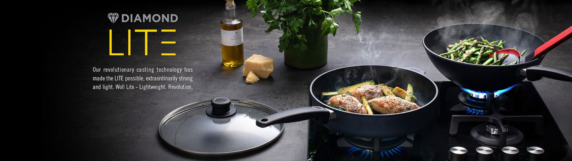 Zwei Diamond Lite Pfannen auf Gasherd mit Essen, daneben Ölflasche, Käse und Kräuter im Hintergrund