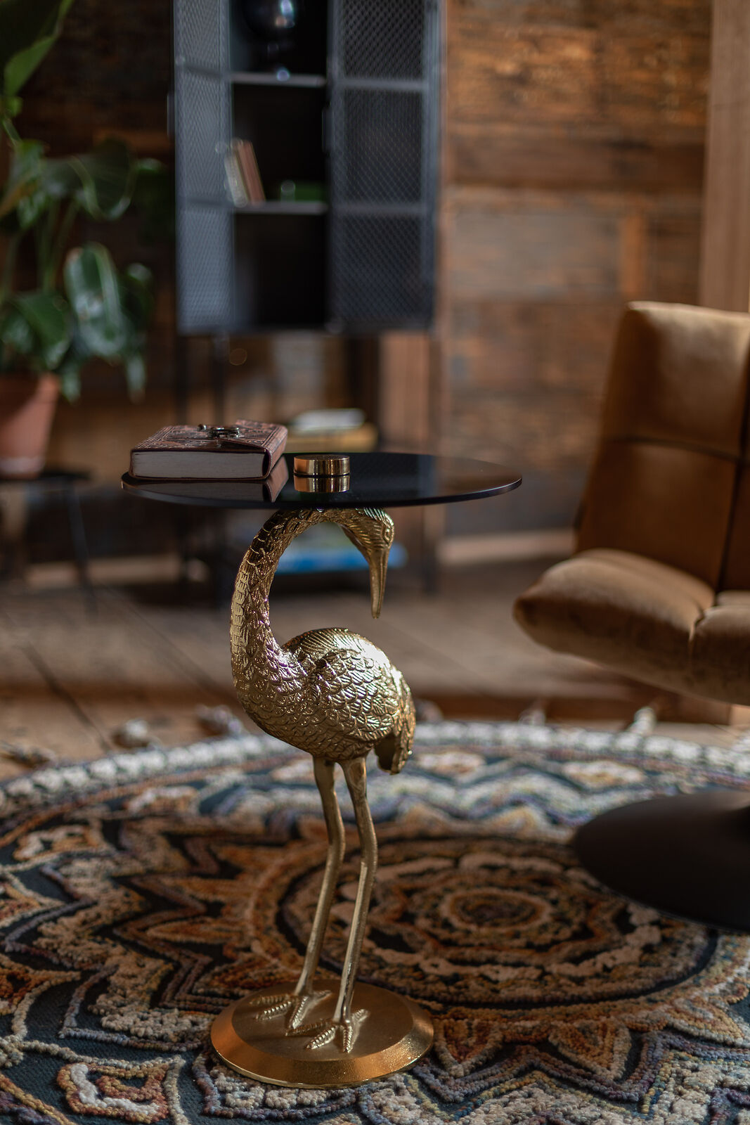 Eleganter Beistelltisch mit Vogelmotiv Beistelltisch mit goldener Vogelfigur als Fuß, darauf ein Buch und eine Kerze, stehend auf gemustertem Teppich.