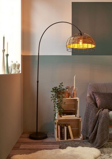 Seitlich aufgenommene Bogenlampe mit braunem Grasoptik-Schirm an schwarzem Gestell über hellem Sofa im modernen Wohnraum