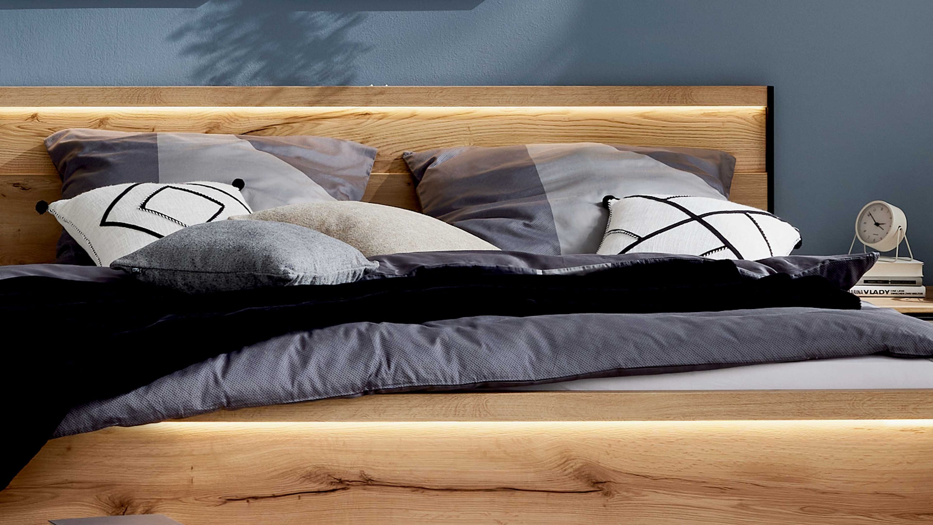 Holzbett mit integrierter Beleuchtung Holzbett mit beleuchtetem Kopf- und Fußteil graue Bettwäsche und Kissen in verschiedenen Grautönen
