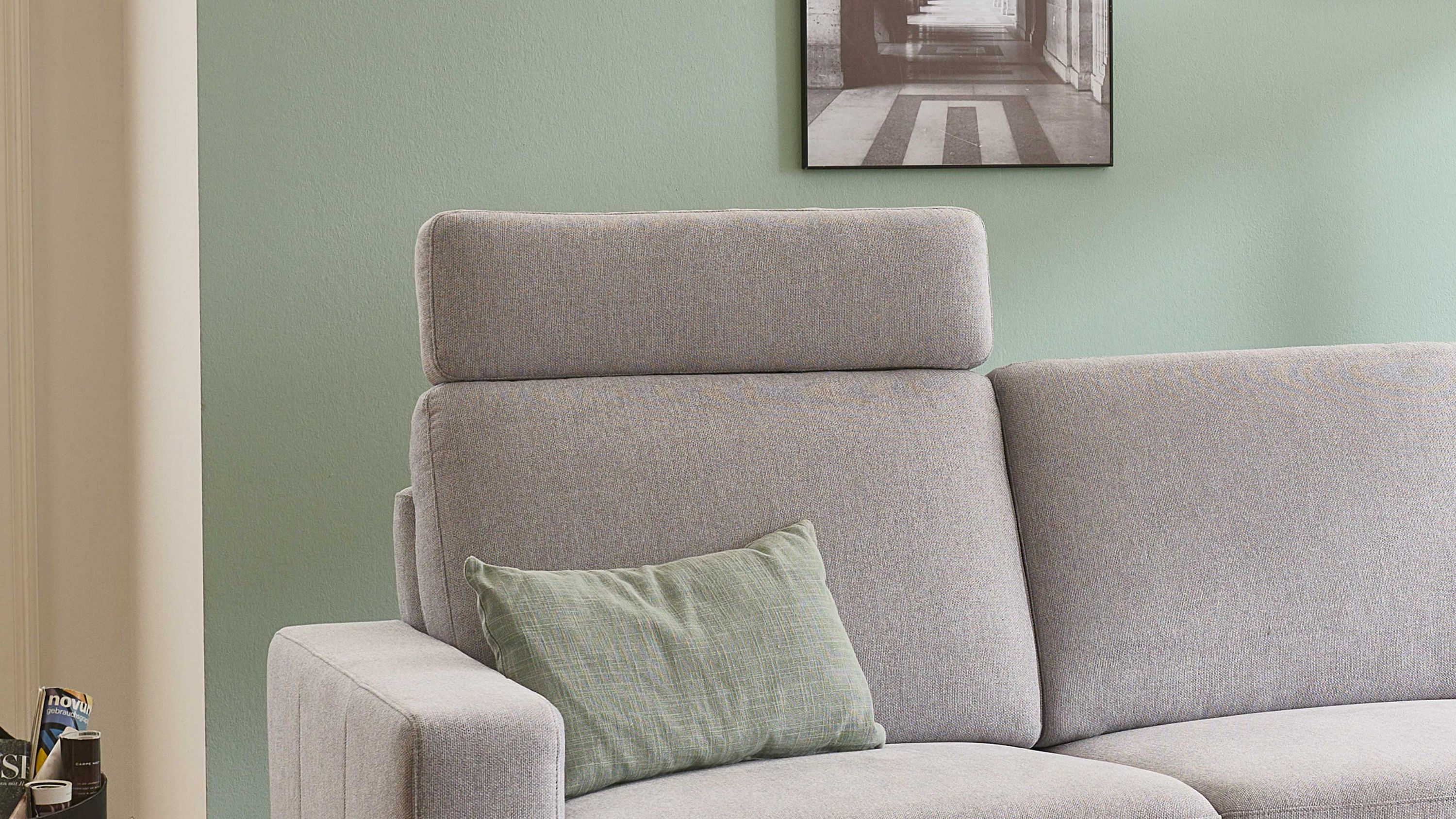 Hellgraue Kopfstütze auf grauem Sofa mit grünem Kissen vor grüner Wand