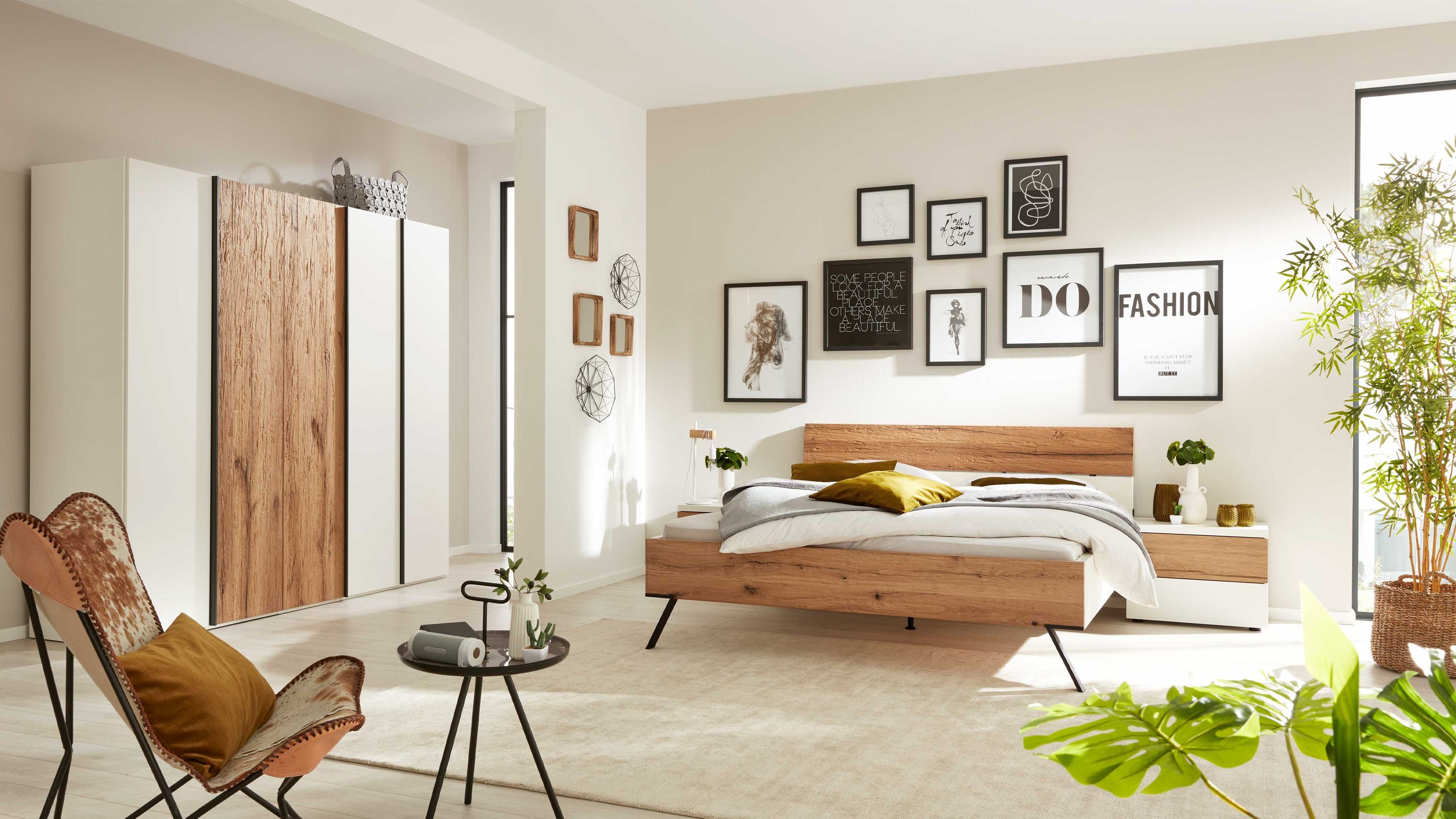 Schlafzimmer mit Bett und Nachttischen in Weiß und Holzfarben Schlafzimmer mit weißem und holzfarbenem Bett zwei Nachttischen und kleinem schwarzen Tisch vor Sessel