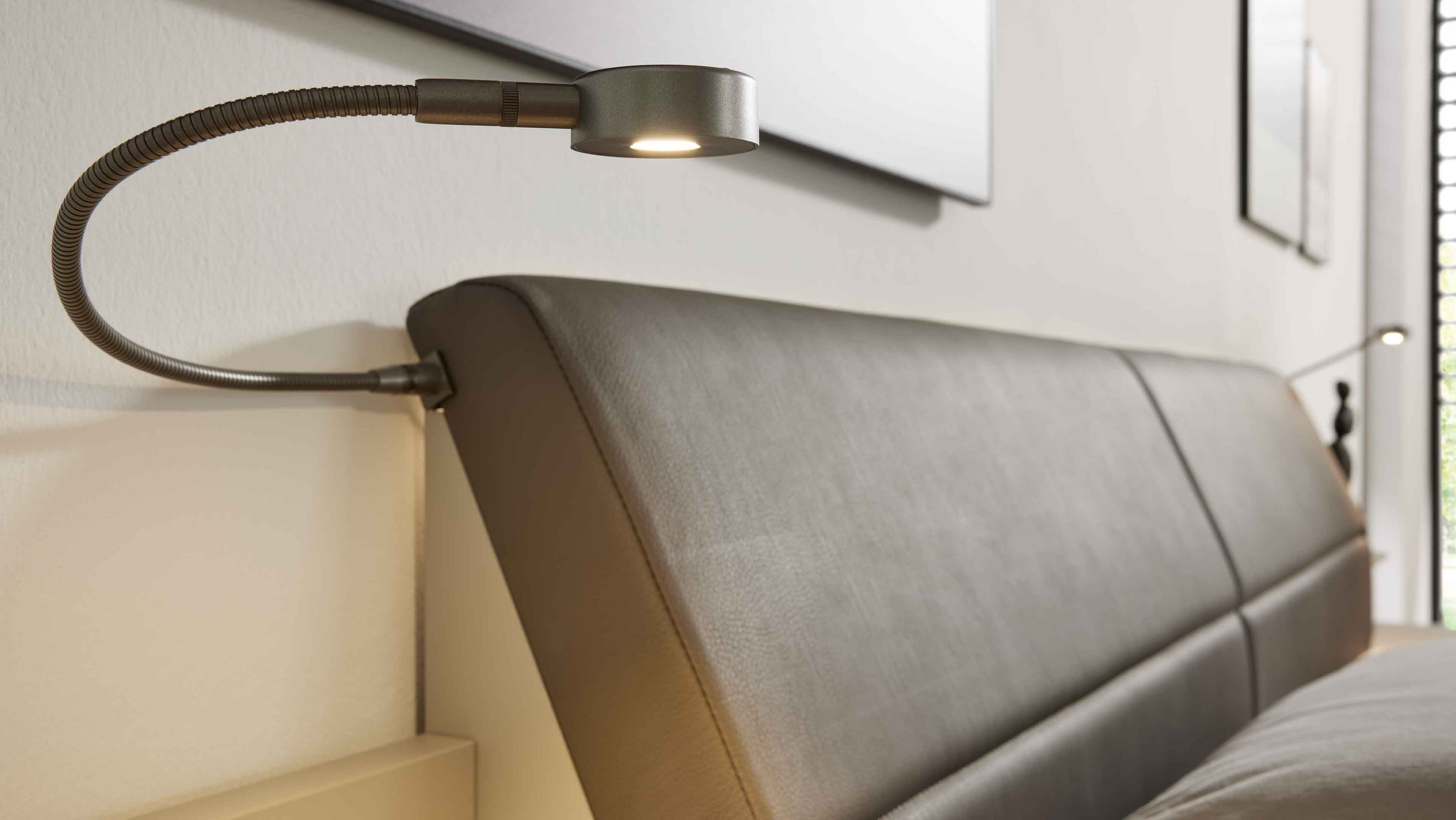 Zweiteiliges Flexleuchten-Set mit gebogenem Arm und rundem Lampenkopf in Metallfarbe an gepolstertem Kopfteil eines Bettes
