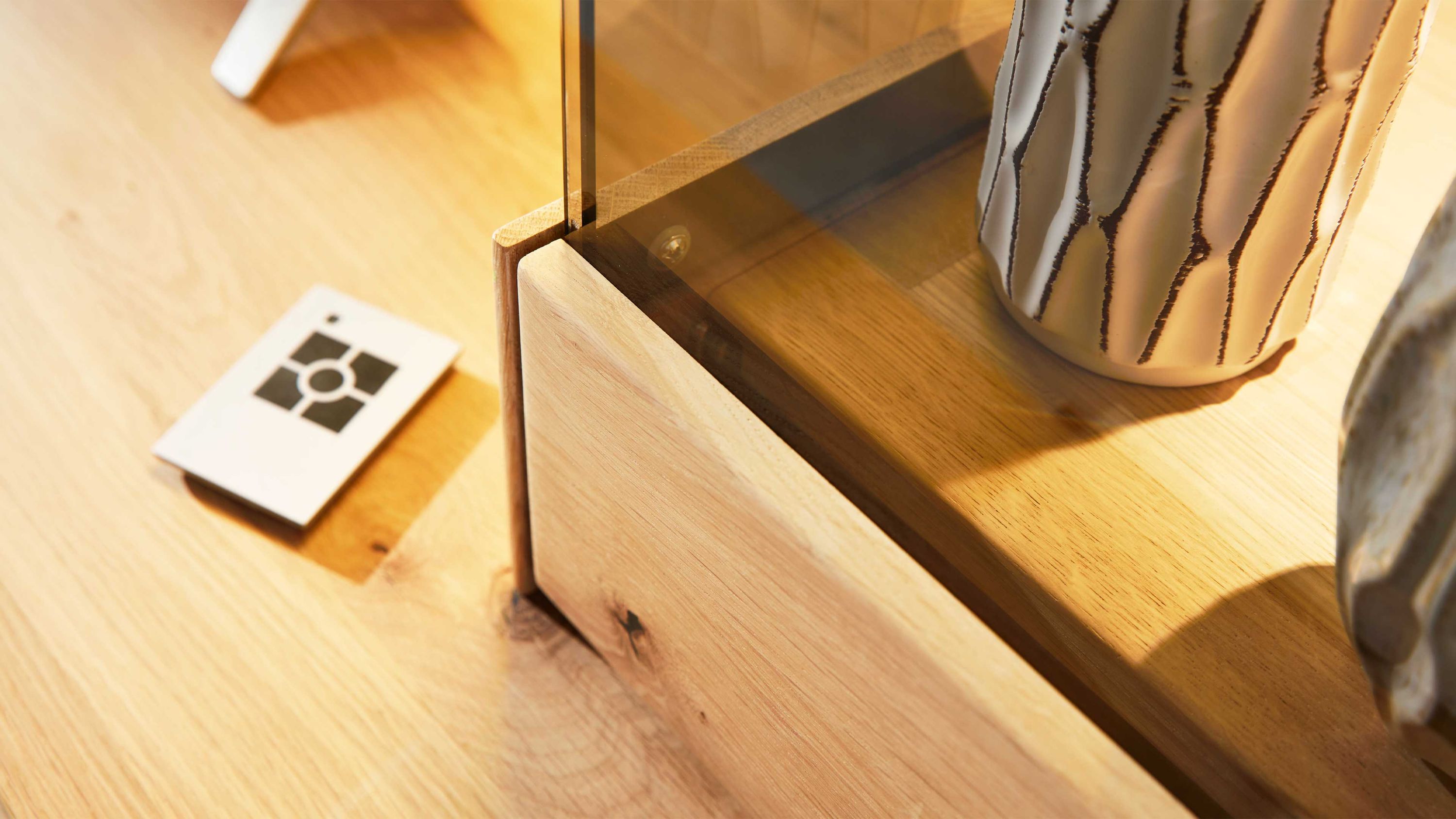 Holzregal mit Glasplatte und weißer Vase mit schwarzem Muster auf hellem Holzboden