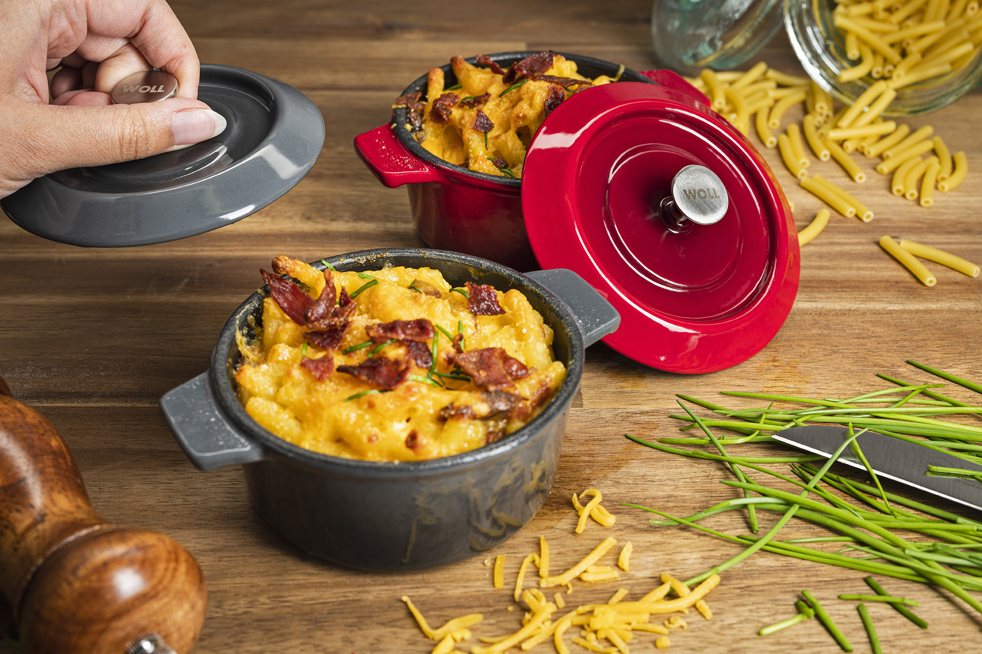 Zwei Mini-Kasserollen auf Holztisch eine grau mit offenem Deckel & Auflauf eine rot mit Deckel Pasta Kräuter & Glas
