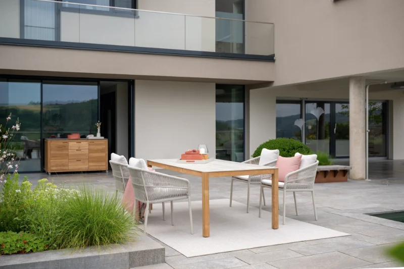 Moderne Terrasse mit großem Esstisch, geflochtenen Gartenstühlen und Sitzbereich vor architektonischem Wohnhaus.