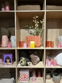 Verschiedene Deko-Artikel wie Kissen, Kerzenhalter und Lampen der Marke Trendhopper in den Farben Pink, Orange und Grau, stilvoll arrangiert.