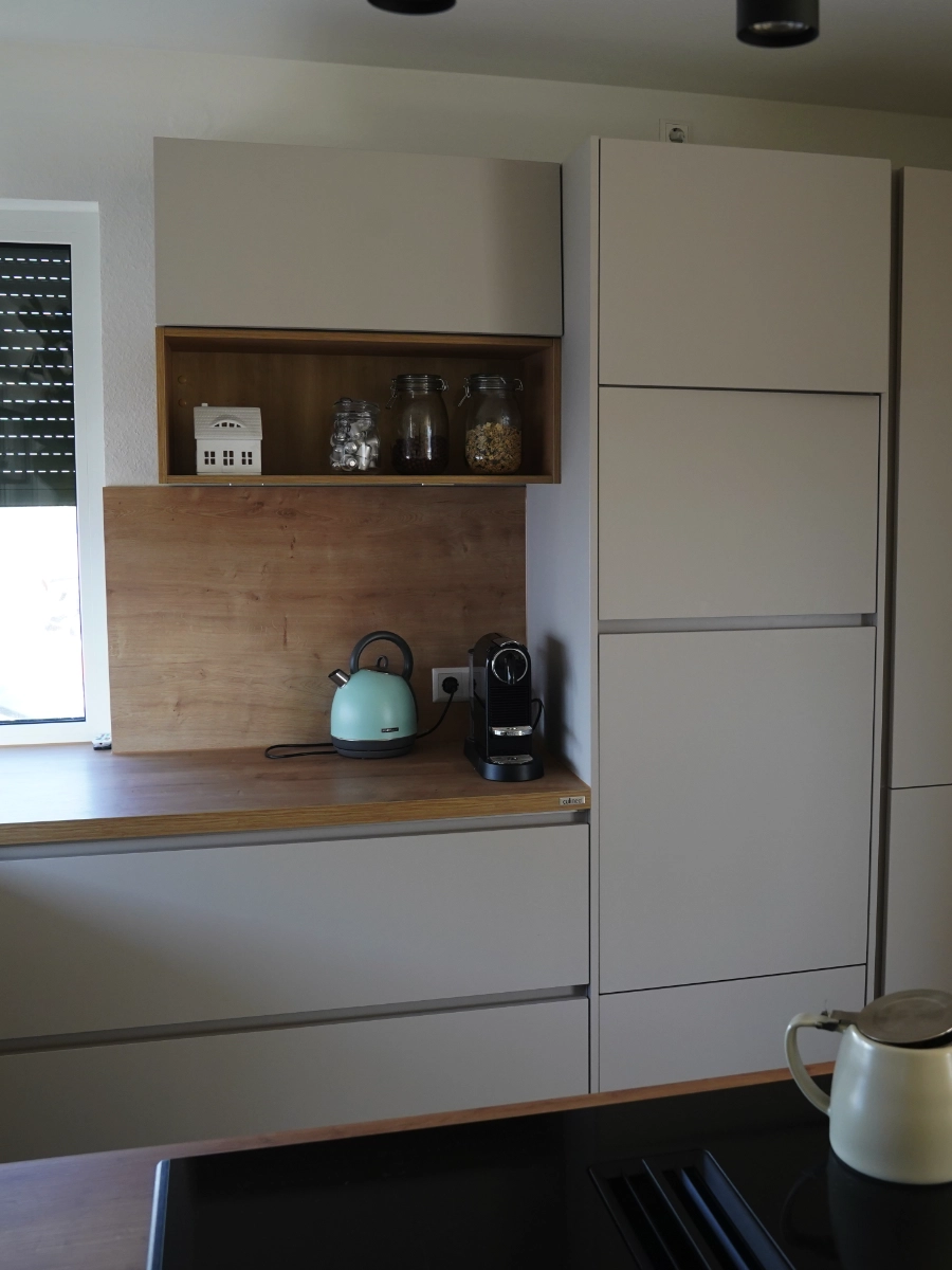 Moderne Wohnküche mit grauer Kochinsel, Holzarbeitsplatte, Induktionskochfeld, Spüle, Hängelampe und großen Fenstern.