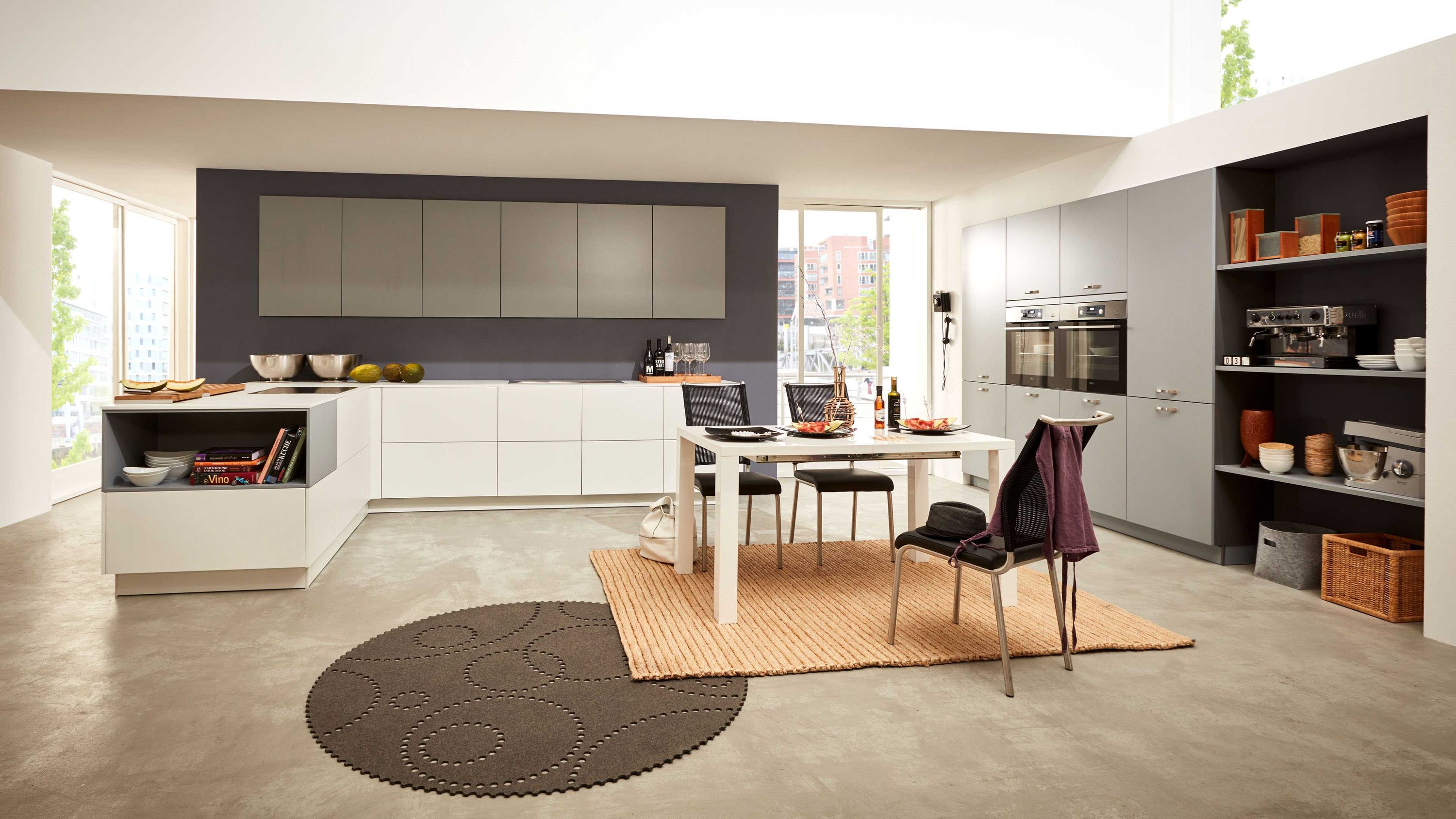 Minimalistische Küche mit Essbereich und dunklem Akzent Weiße Küche mit dunkler Rückwand Betonboden rundem Teppich Esstisch mit zwei Stühlen Küchenutensilien.
