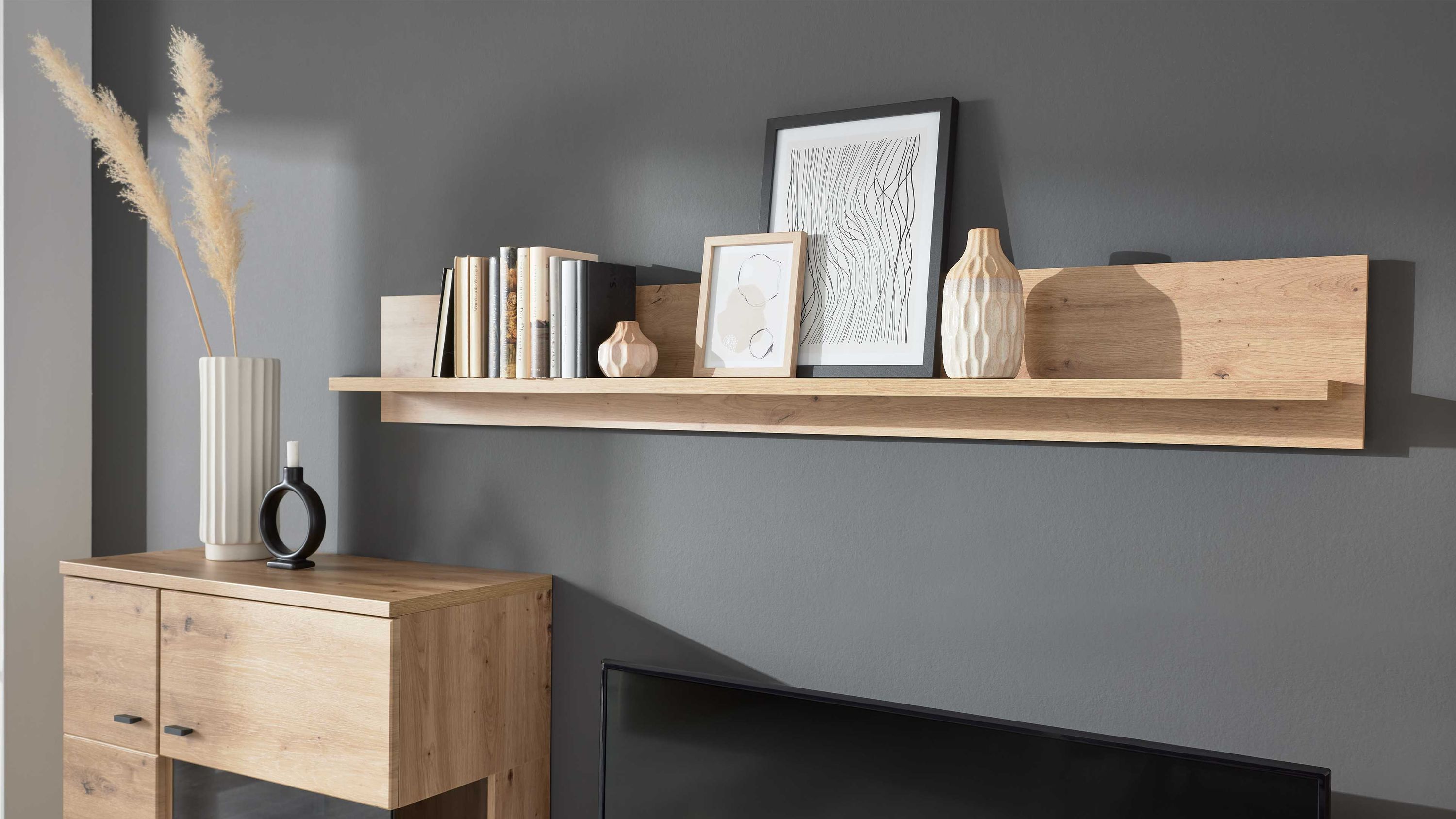 Wandregal aus hellem Holz mit Büchern Vasen und gerahmten Bildern an grauer Wand