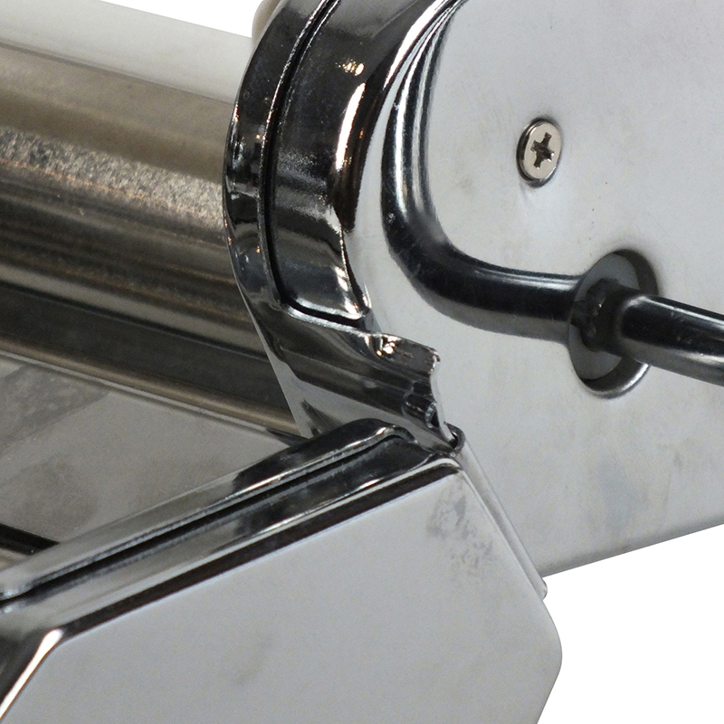 Nahaufnahme einer Nudelmaschine aus Metall mit Walzen und Kurbel, schräg von vorne fotografiert.