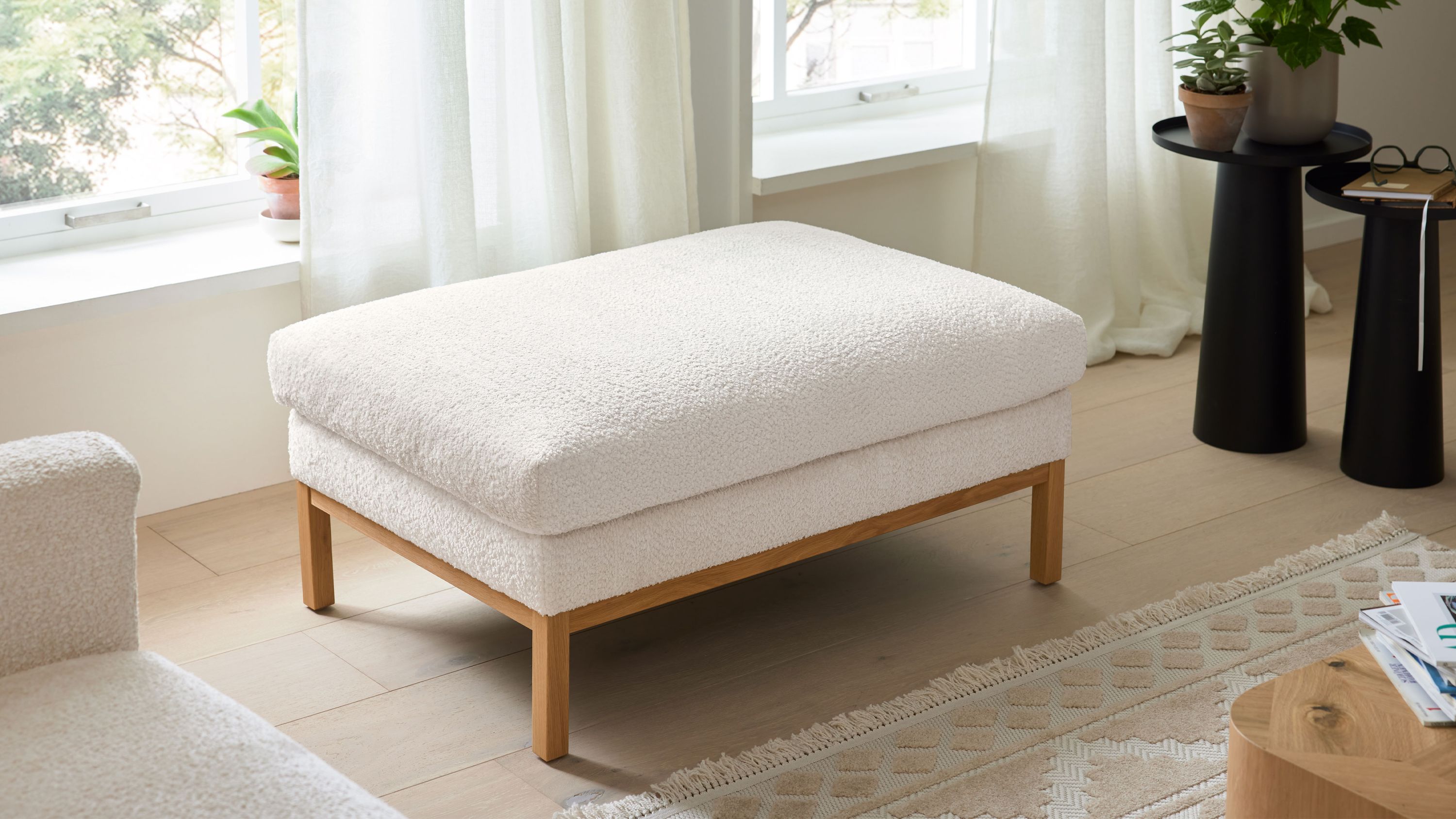 Rechteckiger Polsterhocker mit weißem Stoffbezug und Holzfüßen Rechteckiger Polsterhocker mit weißem Stoffbezug und vier Holzfüßen in einem hellen Wohnzimmer