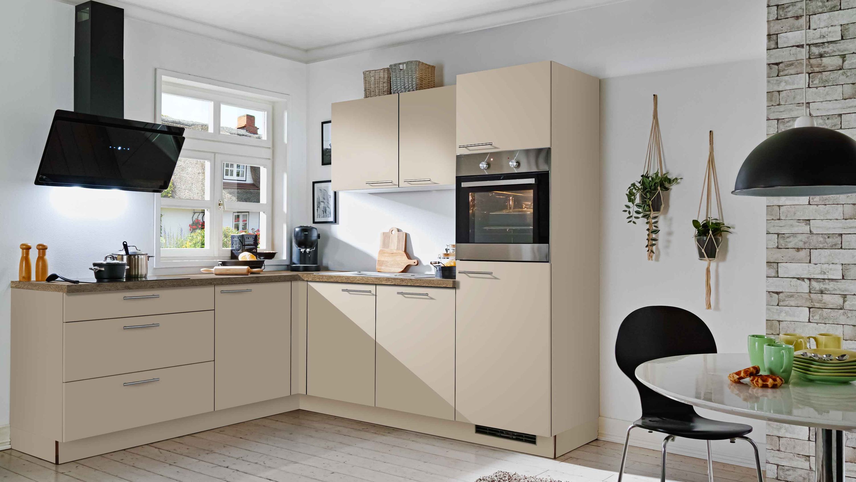 Beige L-Küche mit Essplatz und Backsteinwand Beige L-Küchenfronten schwarze Dunstabzugshaube Einbauofen; runder Tisch mit Lampen Backsteinwand mit Pflanzen
