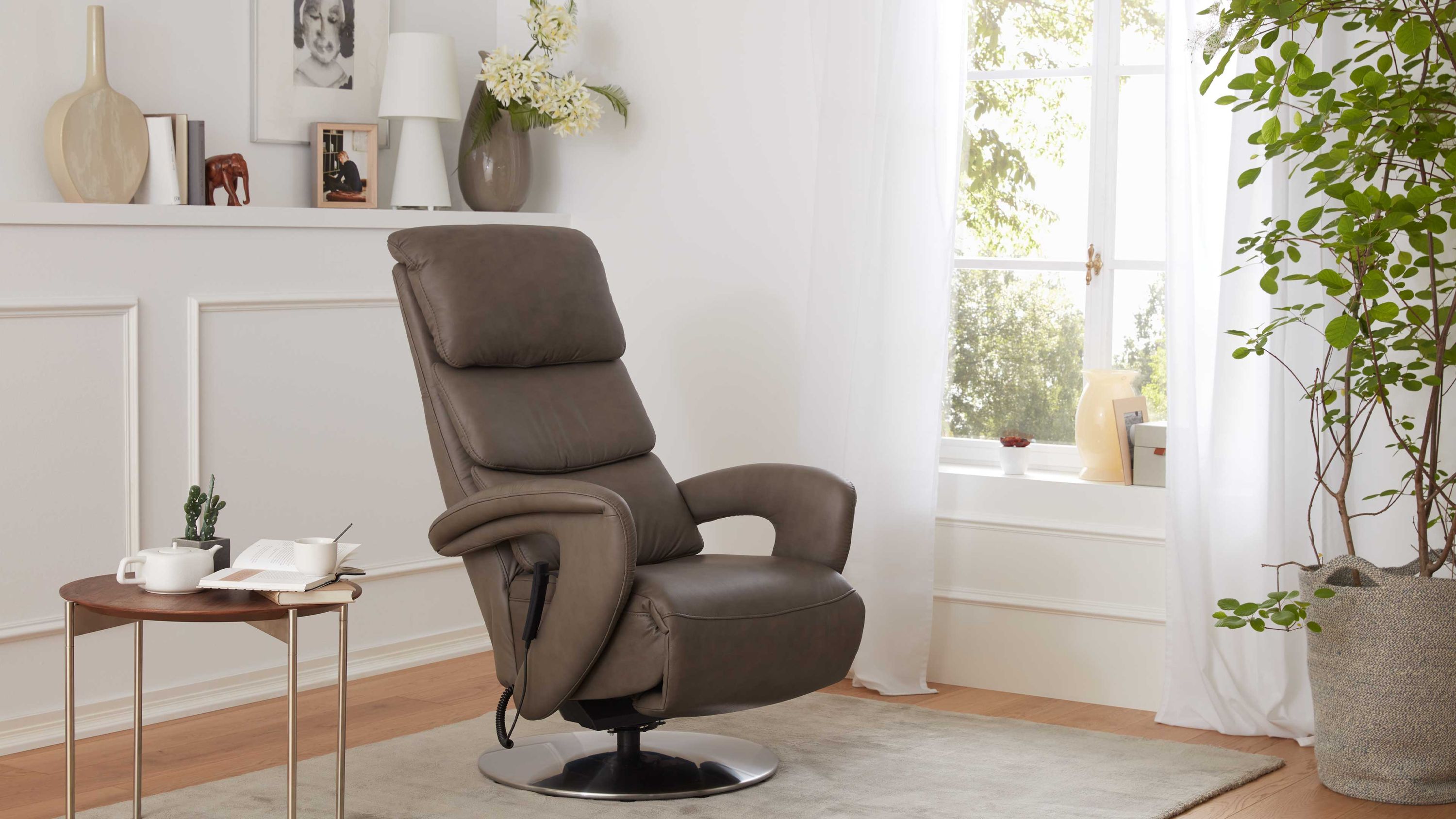 Grauer Relaxsessel mit gepolsterten Armlehnen und rundem Metallfuß in hellem Wohnzimmer