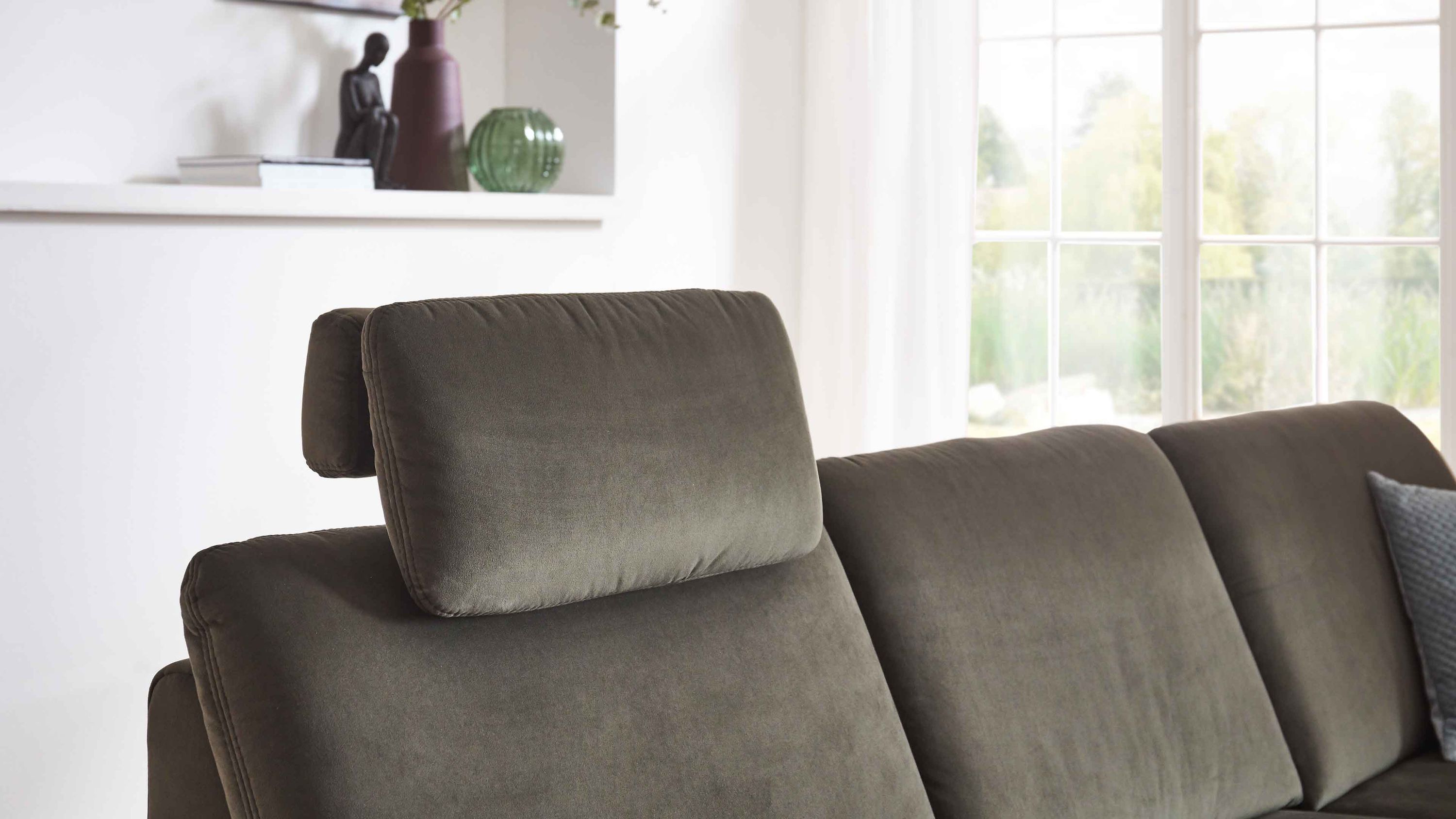 Olivgrüne Kopfstütze auf dunkelgrünem Sofa vor Fenster mit weißen Gardinen