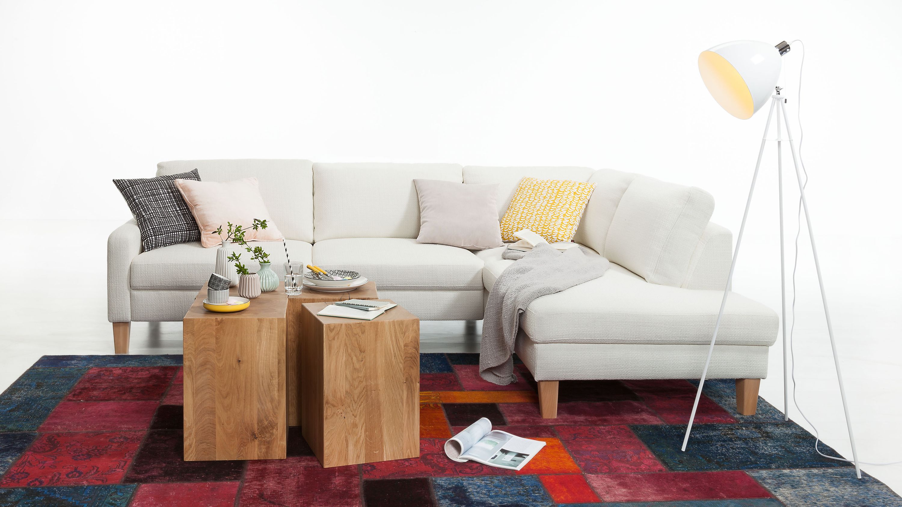 Ecksofa mit cremefarbenem Strukturbezug Holzfüße mehrere Kissen und zwei Holztische davor