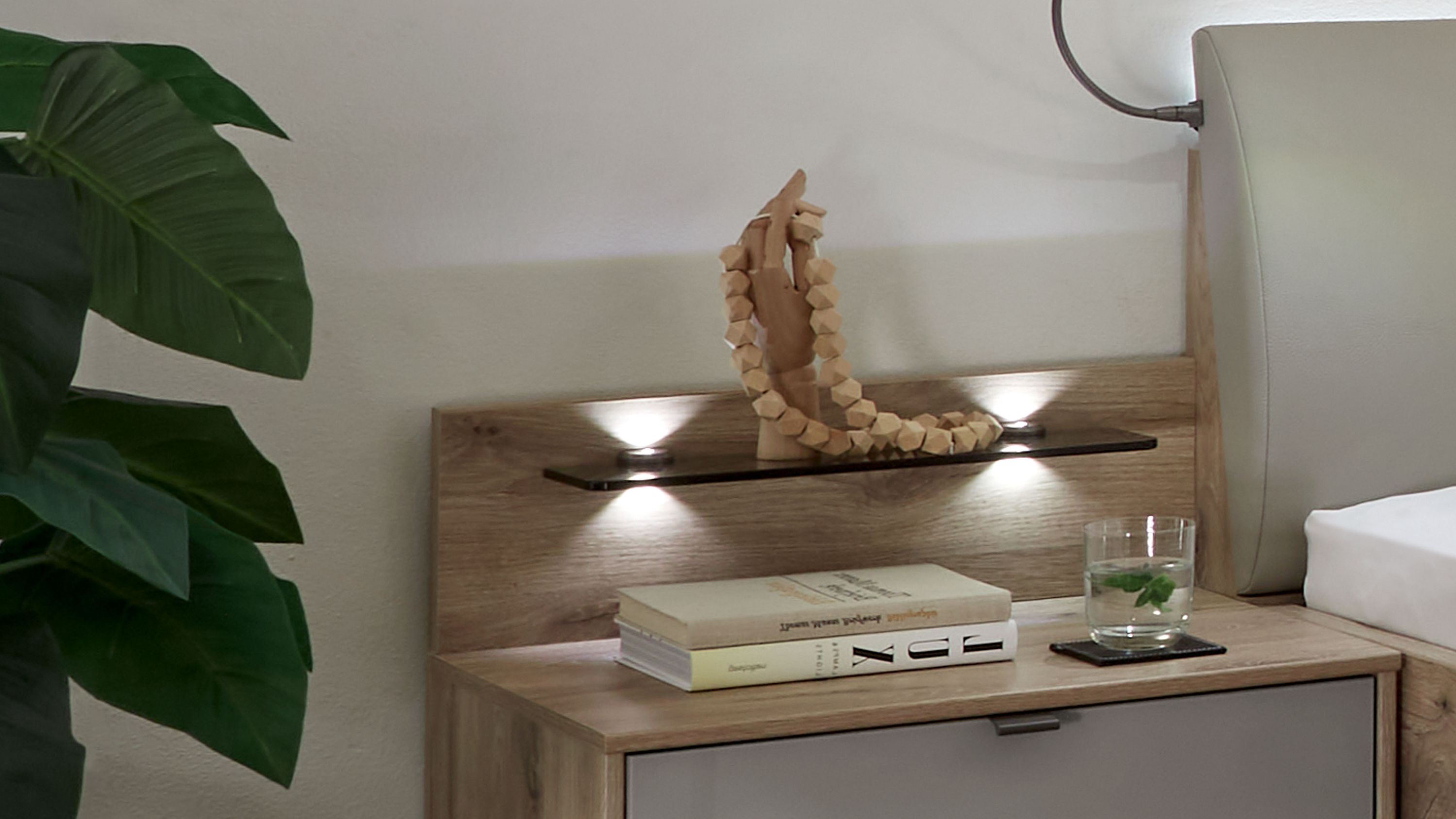 Zweiteiliges Paneelaufsatz mit Holzoptik und Rauchglasablage über Nachttisch mit Büchern und Glas mit Wasser