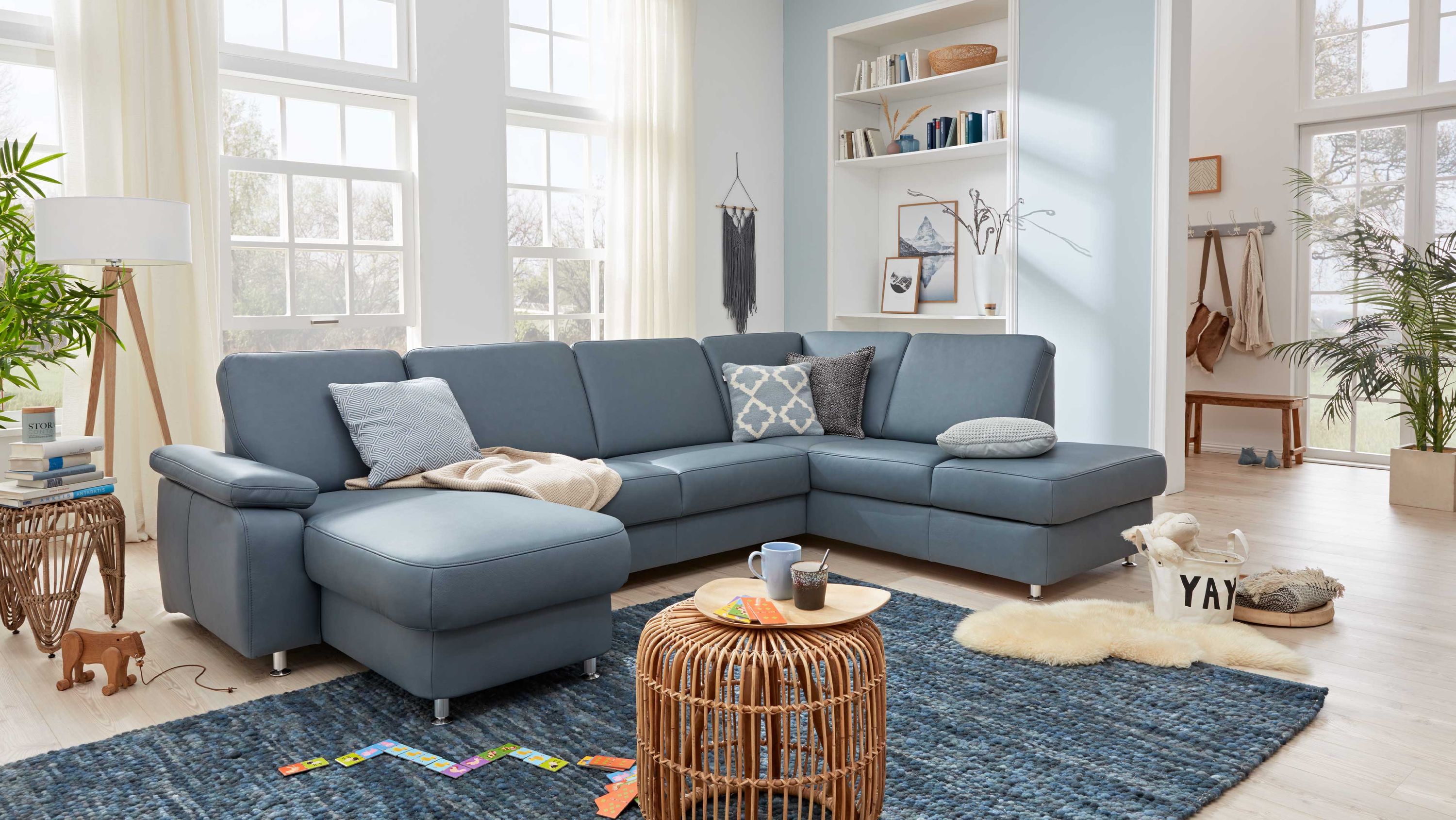 Ecksofa mit stahlblauem Lederbezug und Metallfüßen in hellem Wohnzimmer mit Teppich und Dekokissen