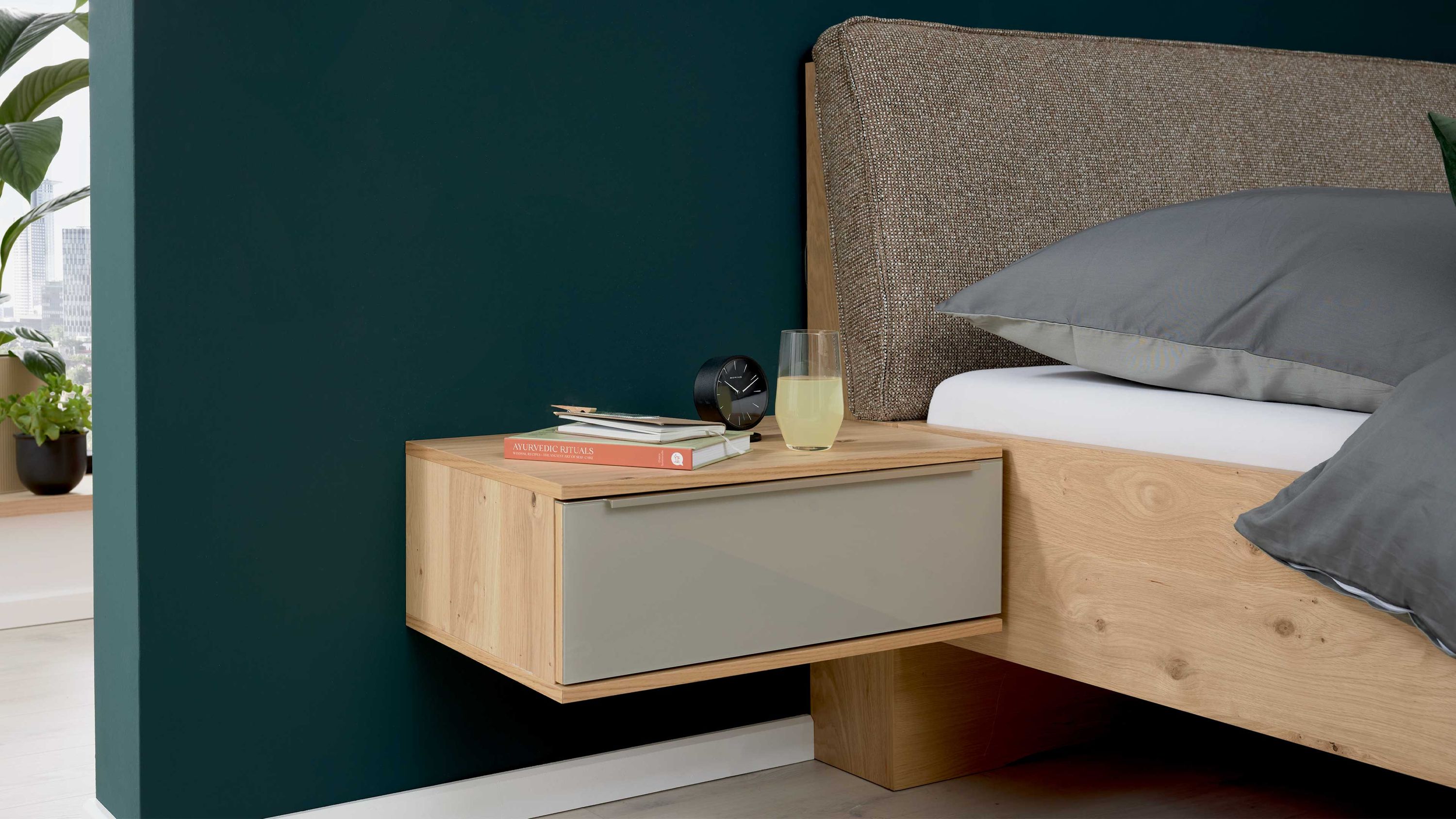 Hänge-Nachtkonsole mit einer Schublade in taupe und Balkeneiche neben einem Bett mit grauem Kopfteil und Kissen