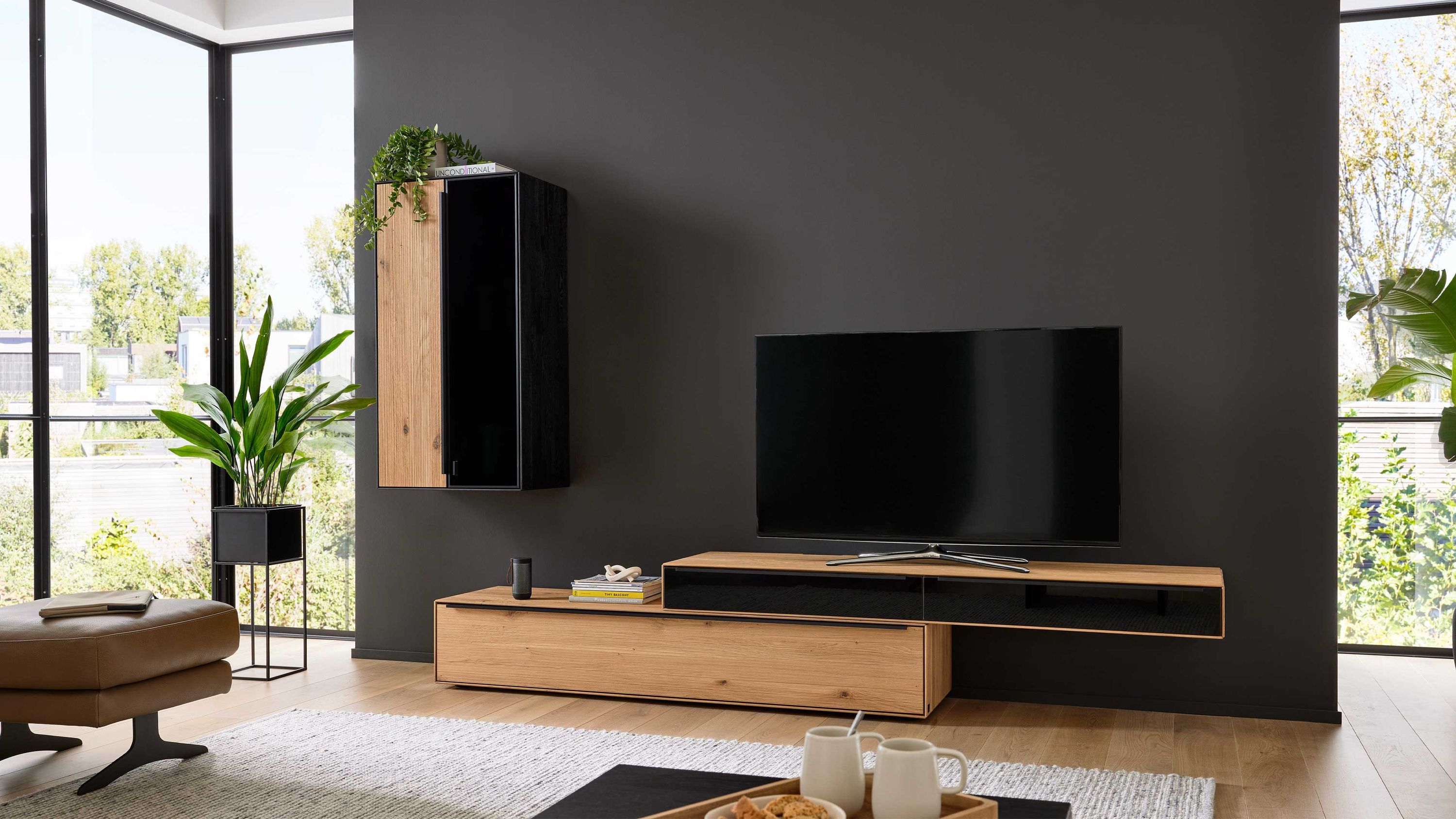 Dreiteilige Wohnwand mit Holz und schwarzen Fronten Dreiteilige Wohnwand mit hellen Holzelementen und schwarzen Fronten an dunkler Wand