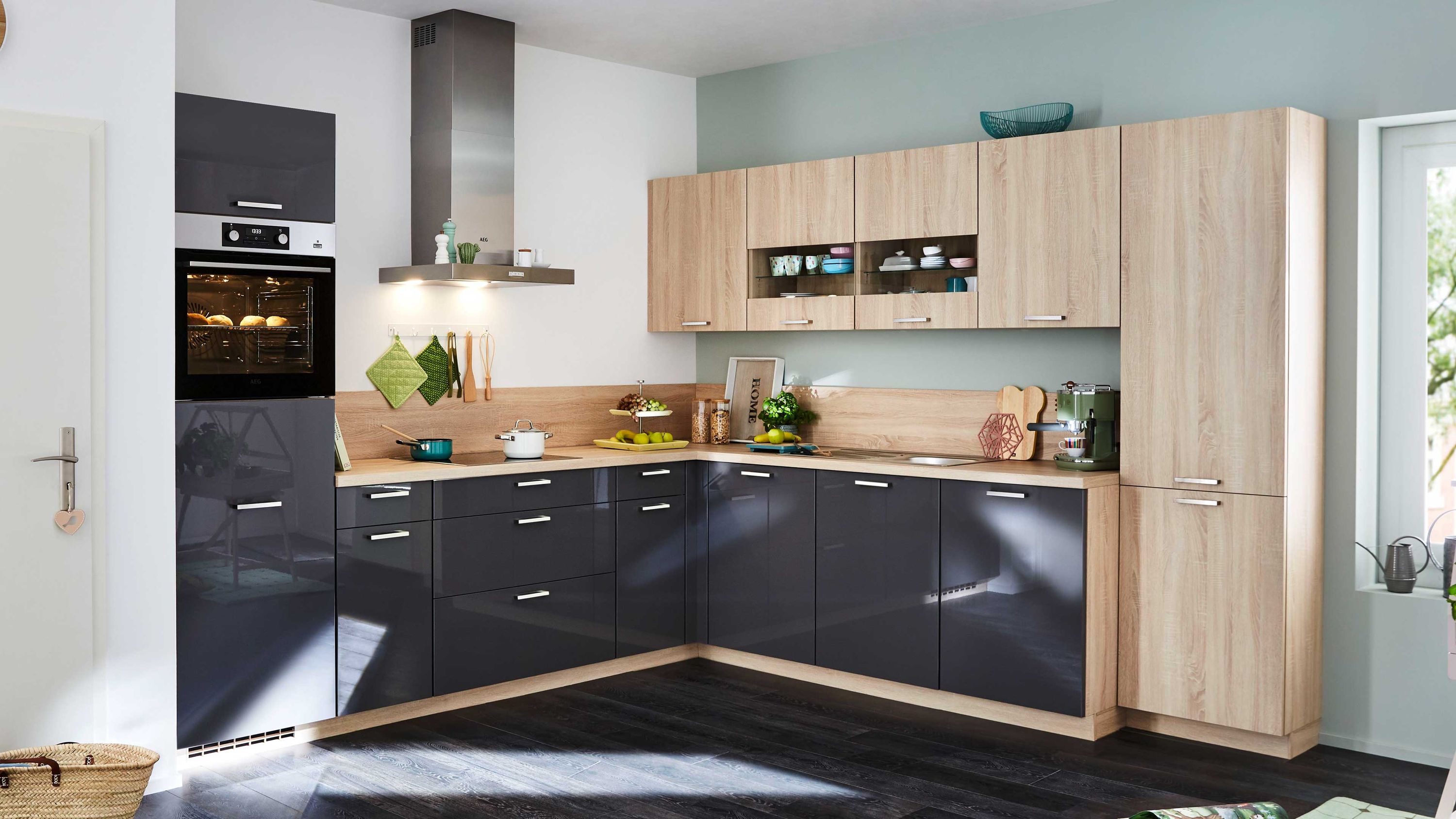 Moderne Küche in L-Form mit grauen Hochglanzfronten und Holzregalen. Ausgestattet mit einem Backofen Kochfeld und verschiedenen Küchenutensilien.