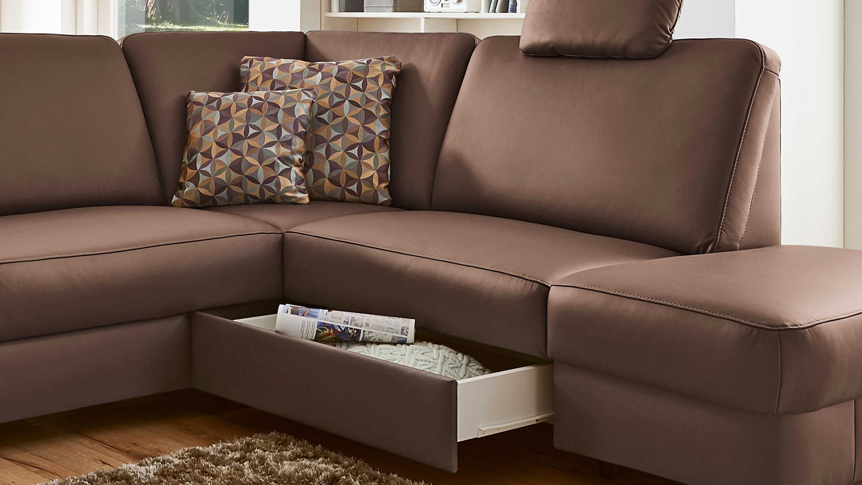 Braunes Ecksofa mit offener Schublade unter der Sitzfläche und zwei gemusterten Kissen