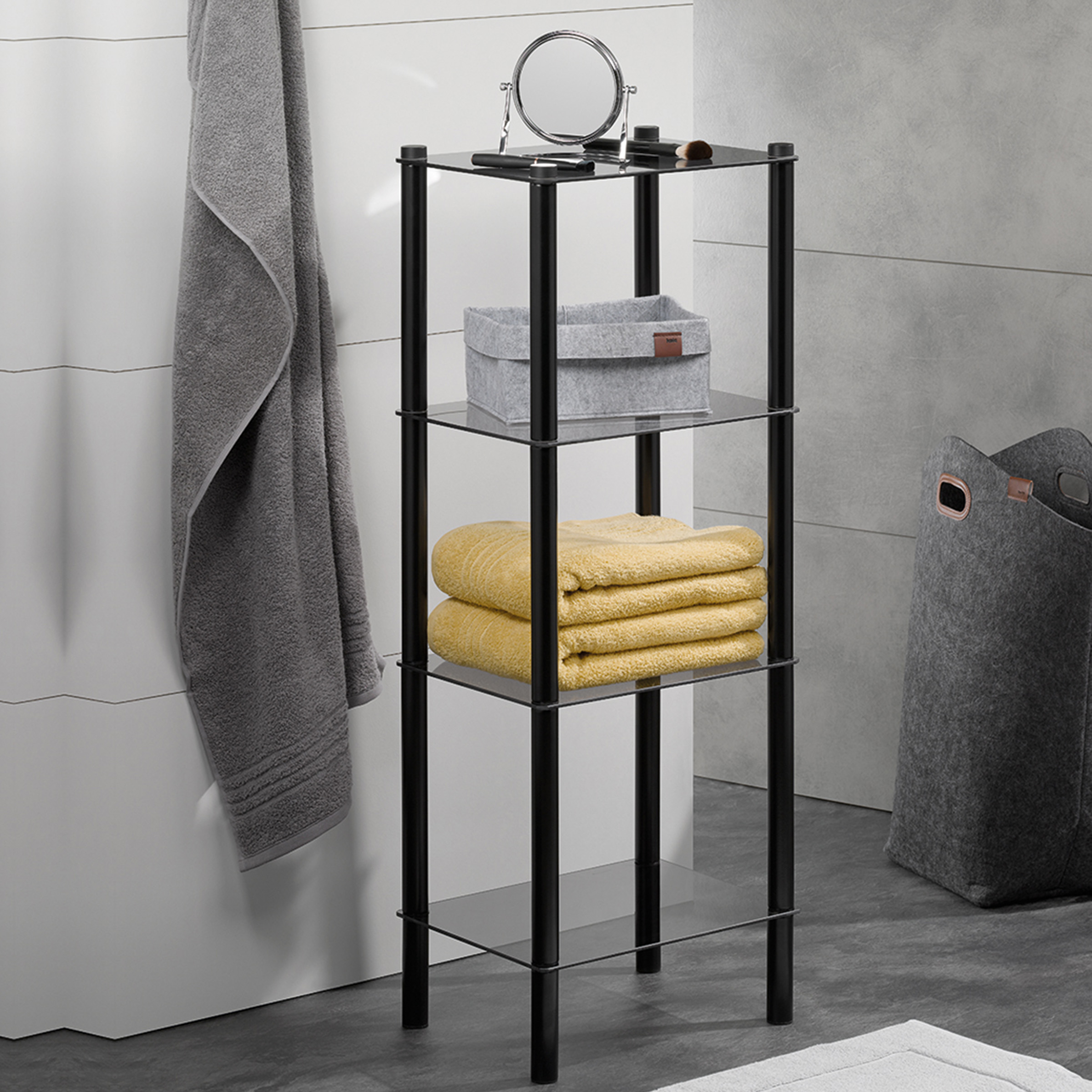 Schwarzes Regal mit vier Glasböden im Badezimmer Schwarzes Regal mit vier Glasböden darauf grauer Korb und gelbe Handtücher steht in modernem Badezimmer