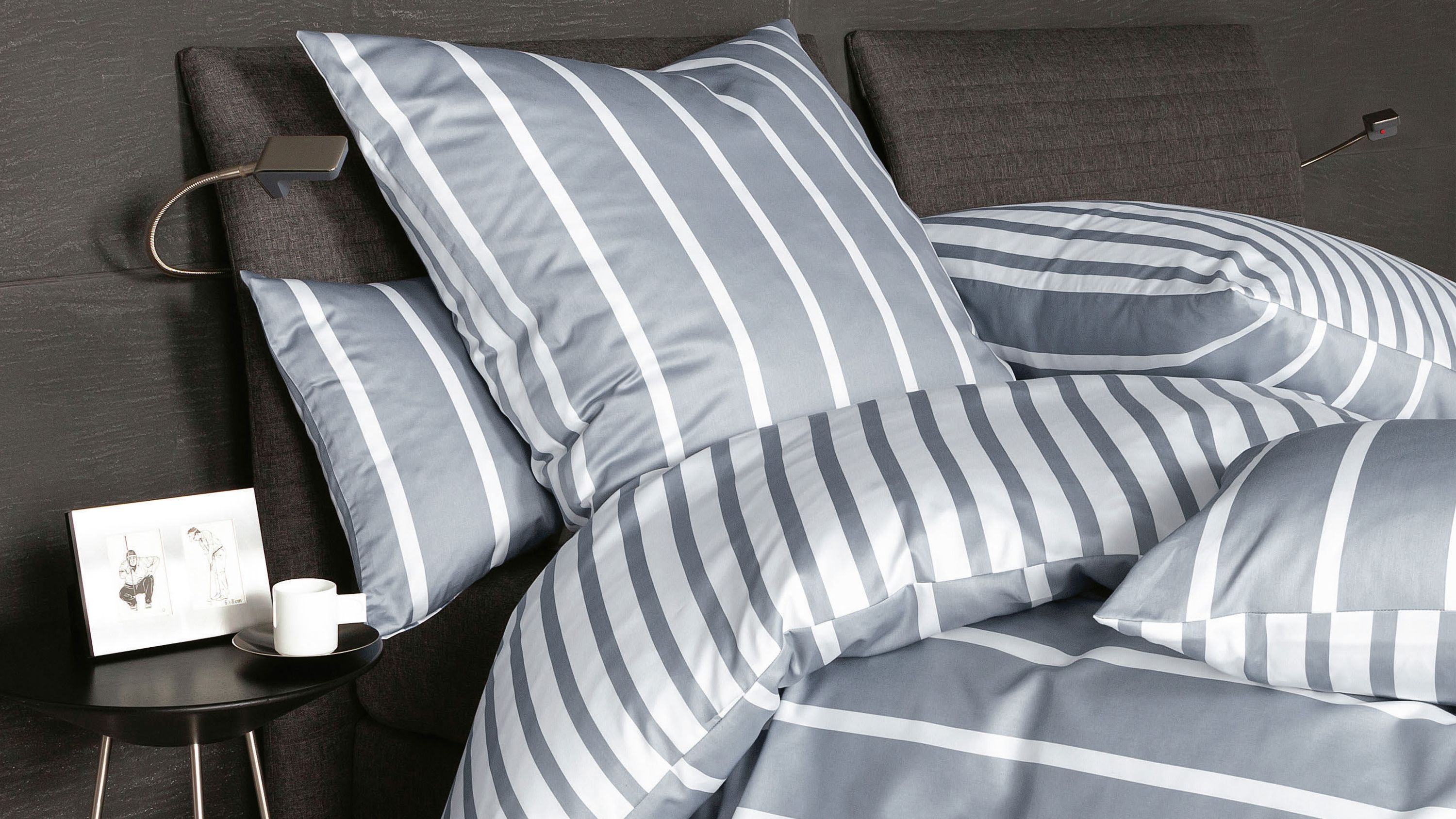 Bett mit grauer und weiß gestreifter Bettwäsche aus Kissen und Decke auf dunklem Kopfteil