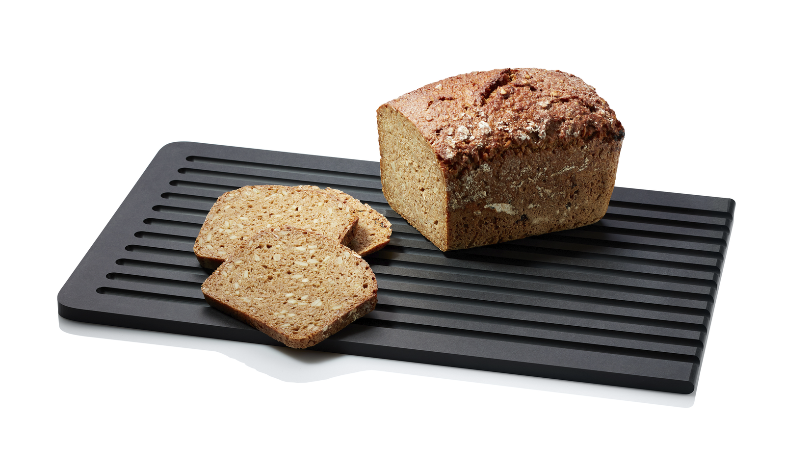 Schwarz gerilltes Schneidebrett mit einem Laib Mehrkornbrot und zwei Brotscheiben auf weißem Hintergrund ausgeleuchtet